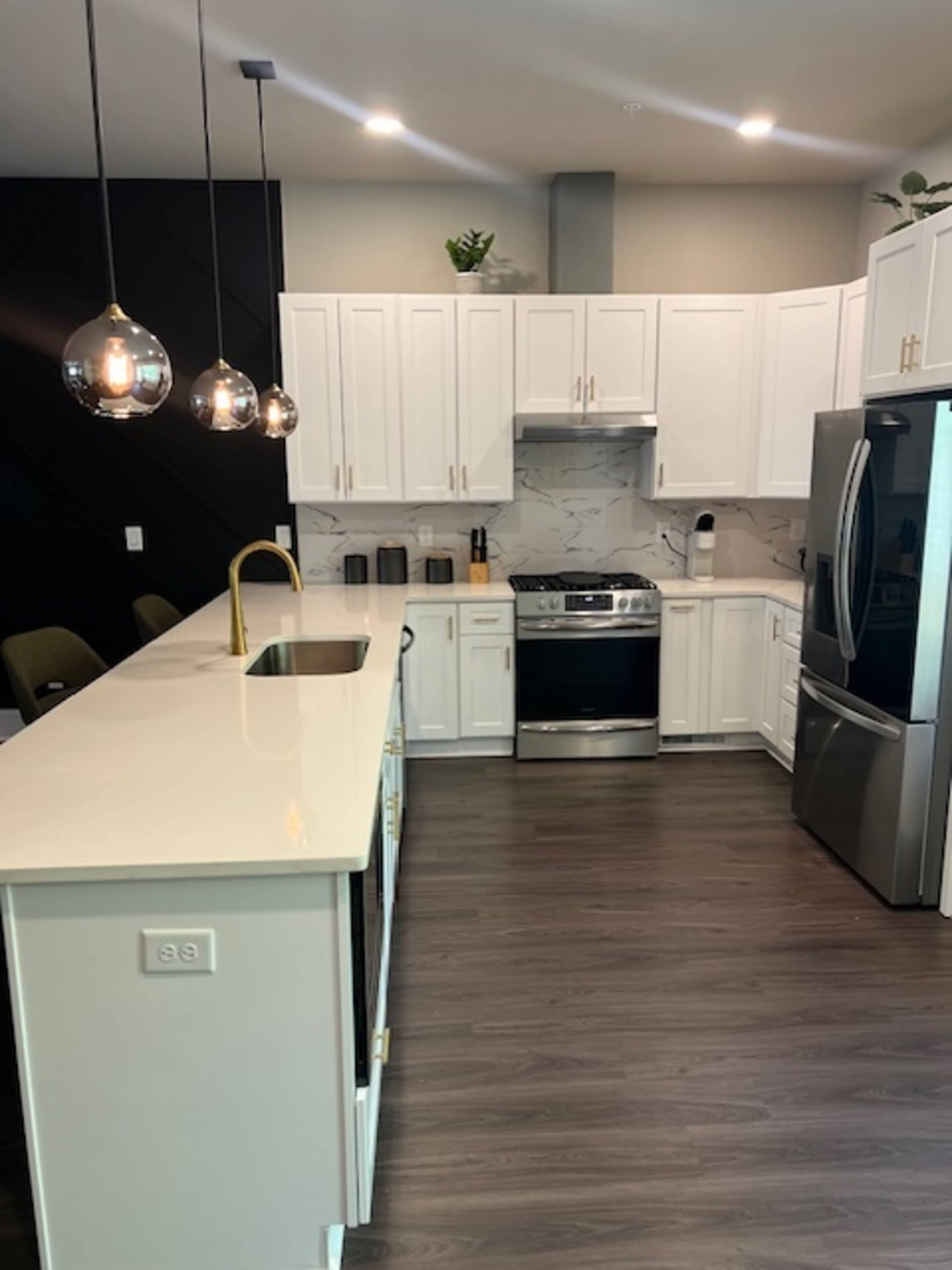 The image shows a modern kitchen with white cabinets, stainless steel appliances, and a large island with a sink and bar seating.