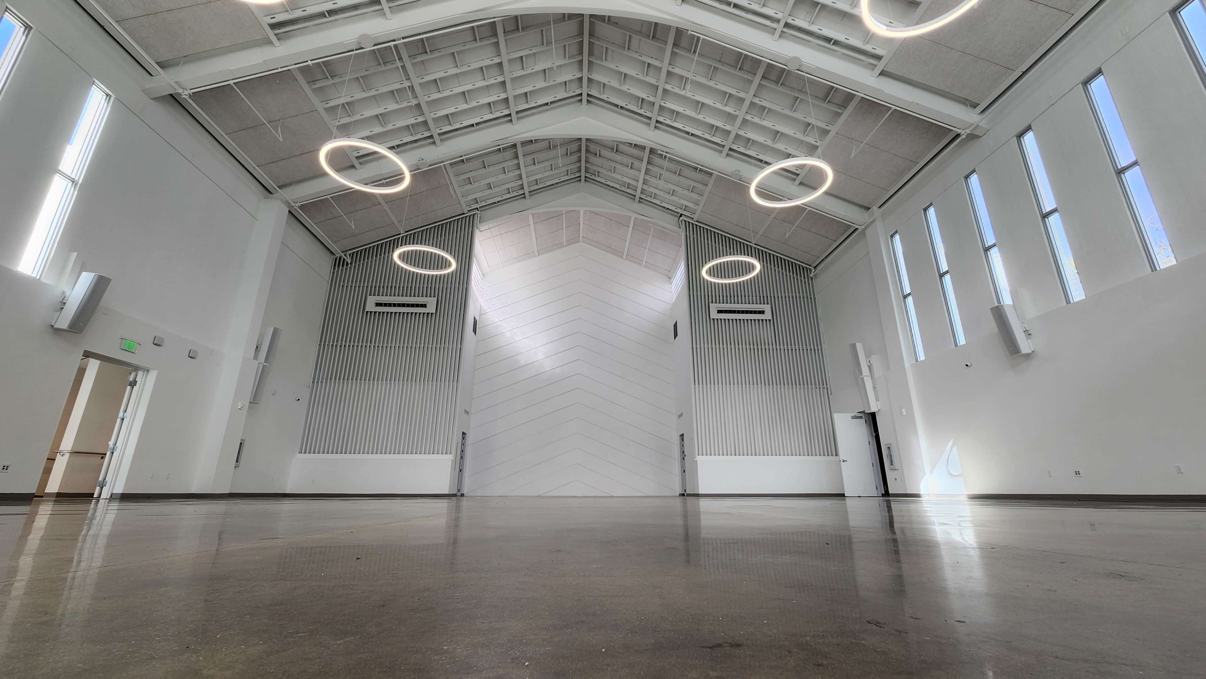 The image shows a modern, spacious room with high ceilings, large windows, and minimalistic design elements.