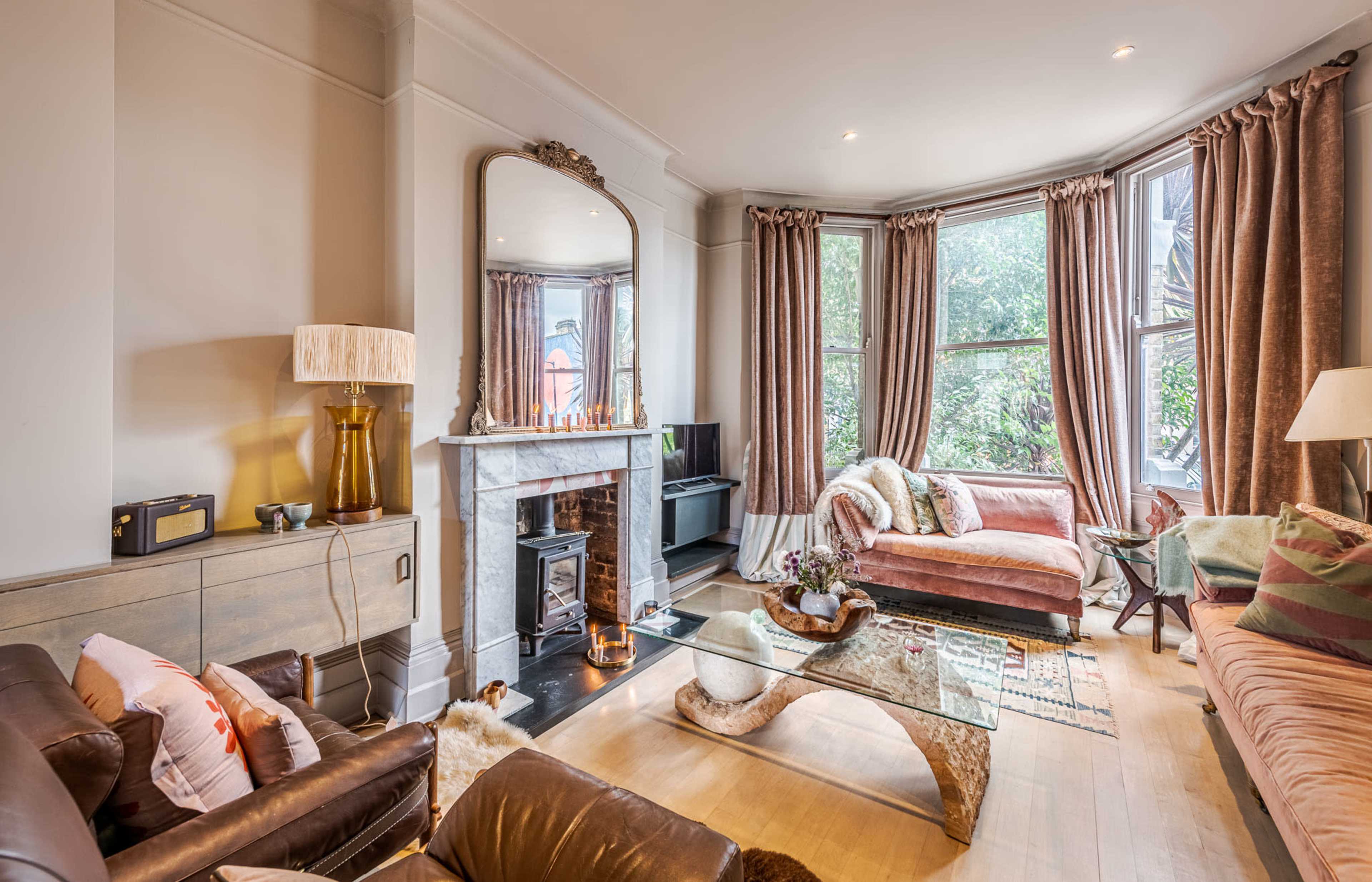The living room features a large bay window, a marble fireplace, and a glass coffee table surrounded by various seating options.