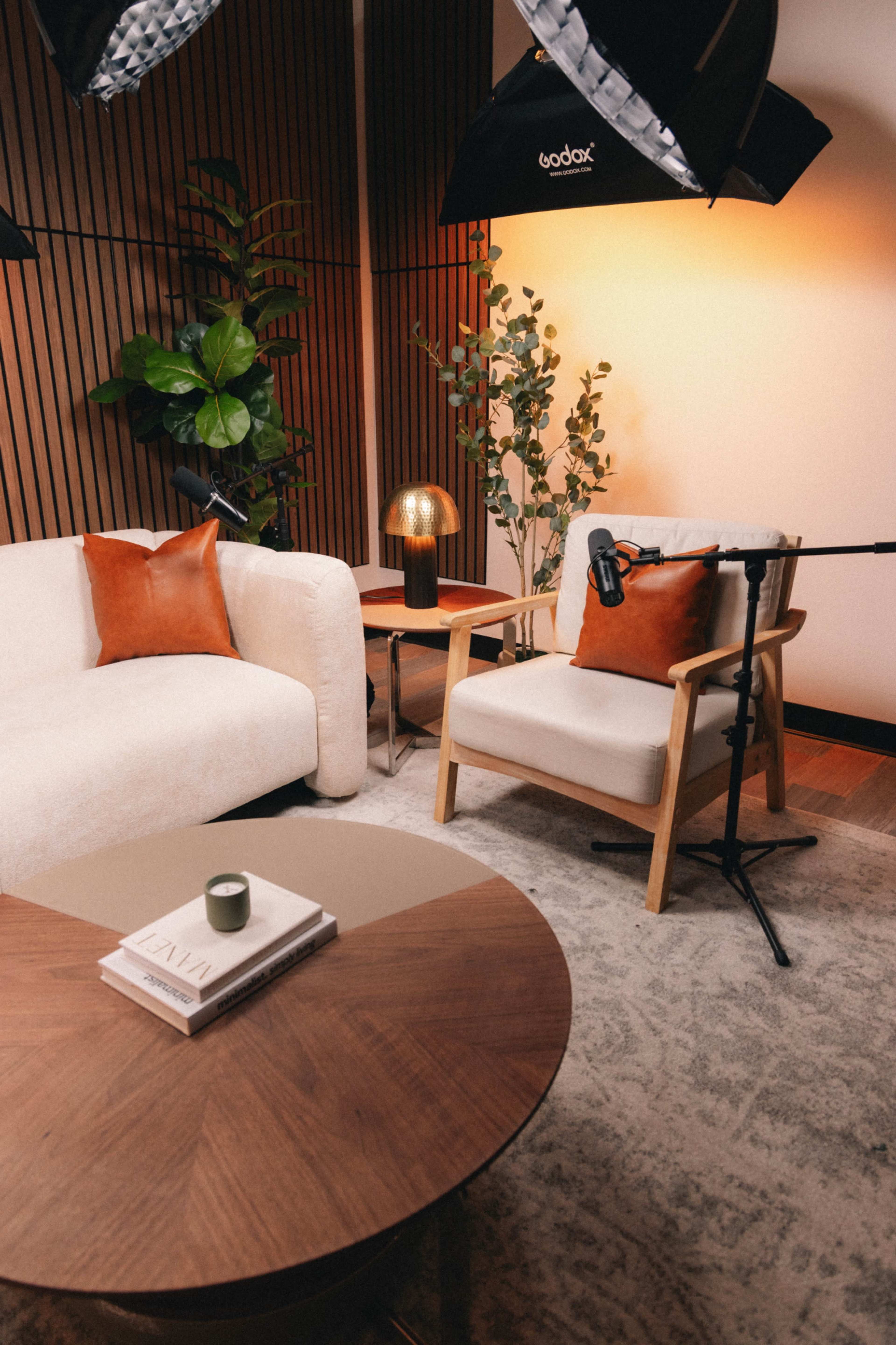 The image shows a stylish living space with a white sofa, a wooden chair, a round coffee table, and potted plants, illuminated by soft lighting.