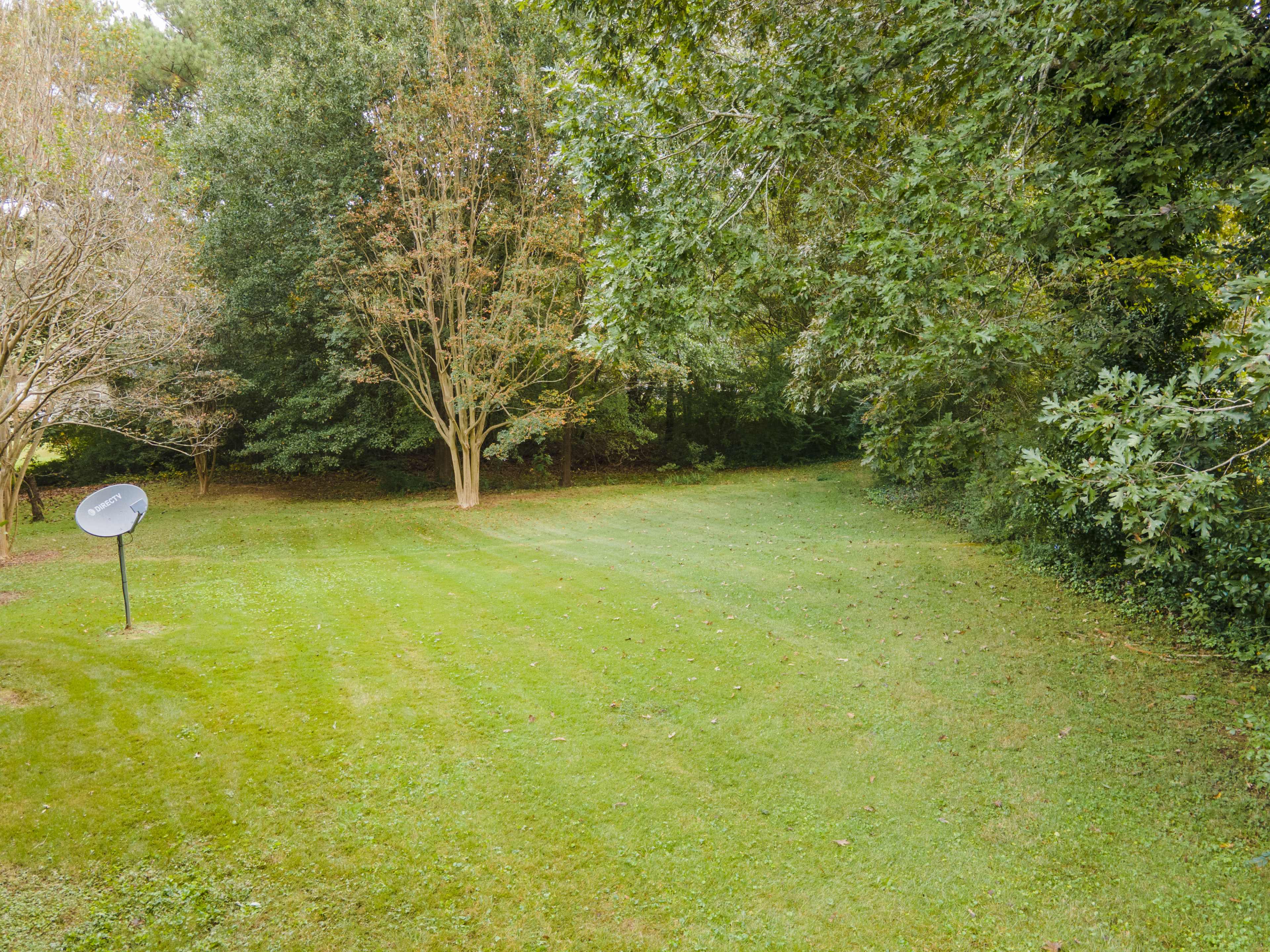 A green lawn is bordered by trees, with a satellite dish standing on a metal pole in the foreground.