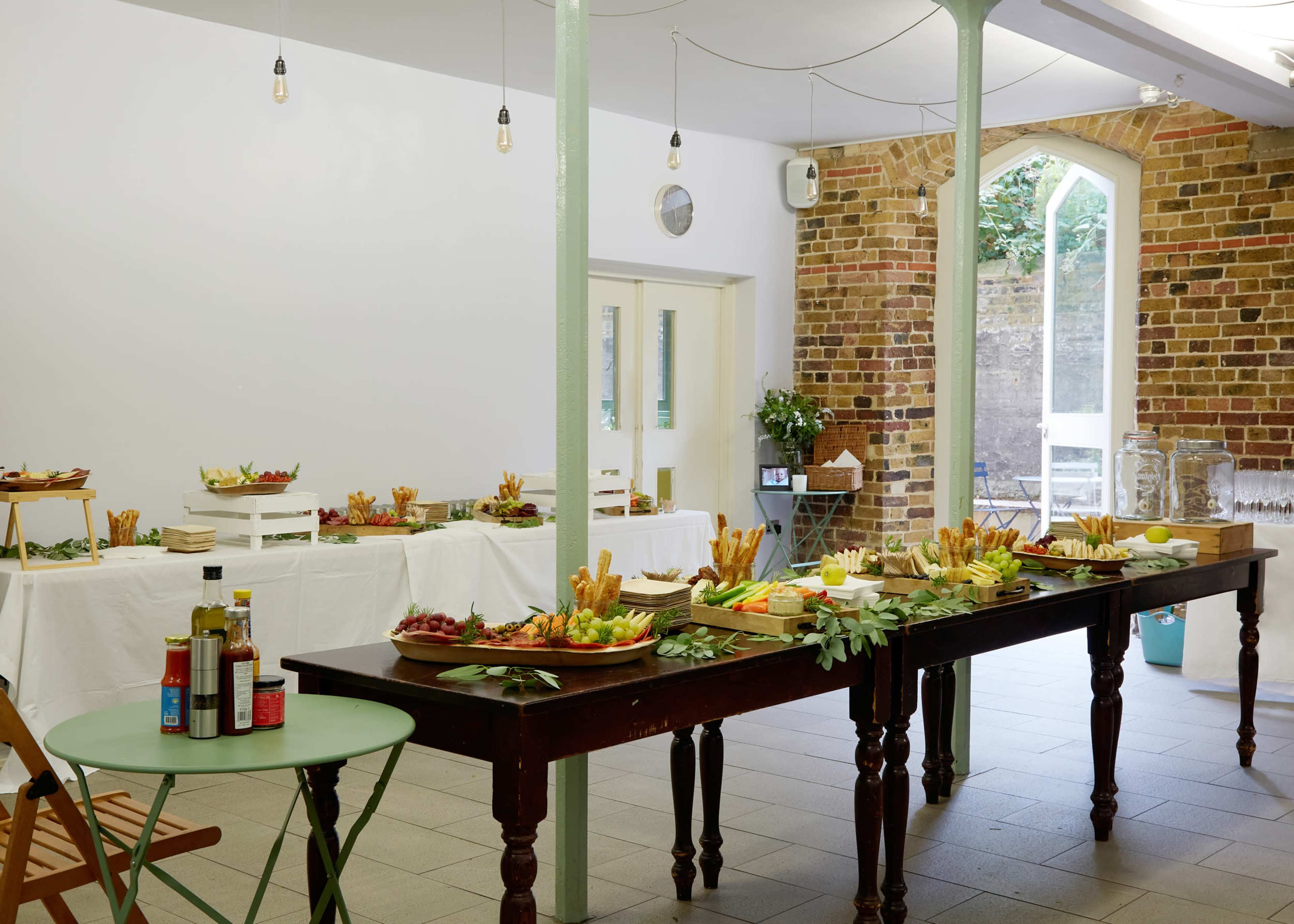 A spacious room features multiple tables set with a variety of platters filled with fruits, vegetables, and snacks.