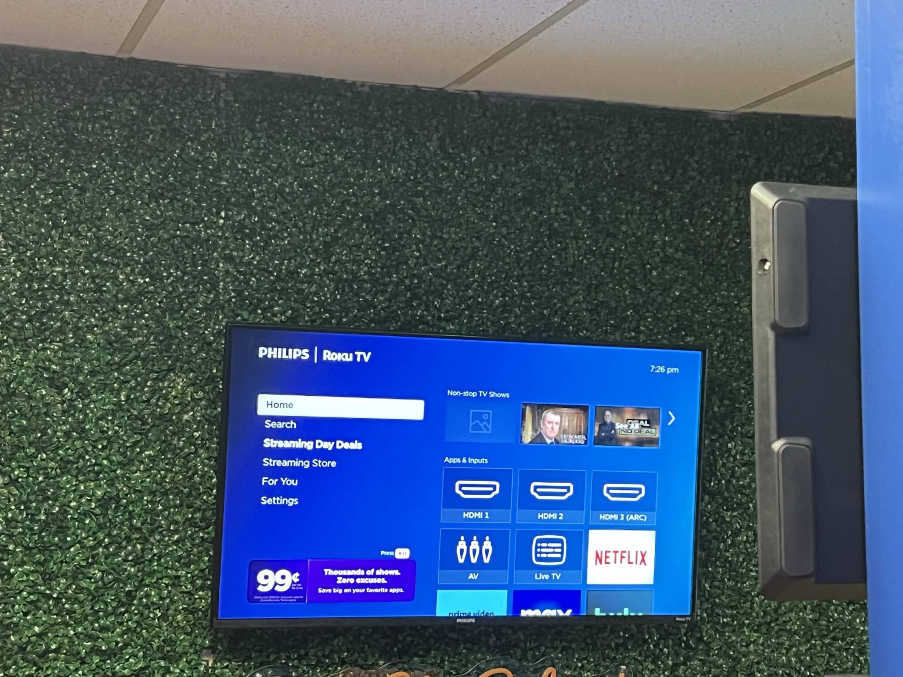 A Philips Roku TV displays a menu featuring search options, streaming deals, and app recommendations on a green backdrop.