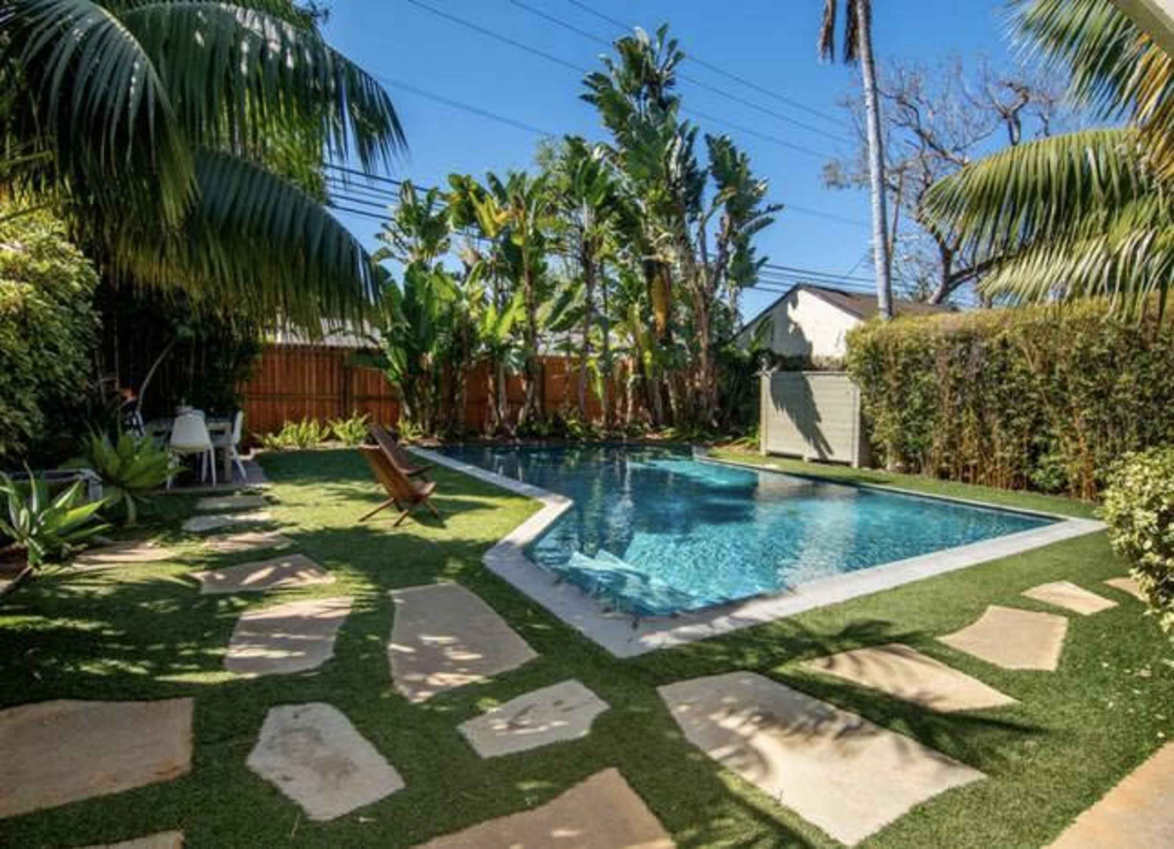 A backyard with a swimming pool surrounded by tropical plants and stone pathways.
