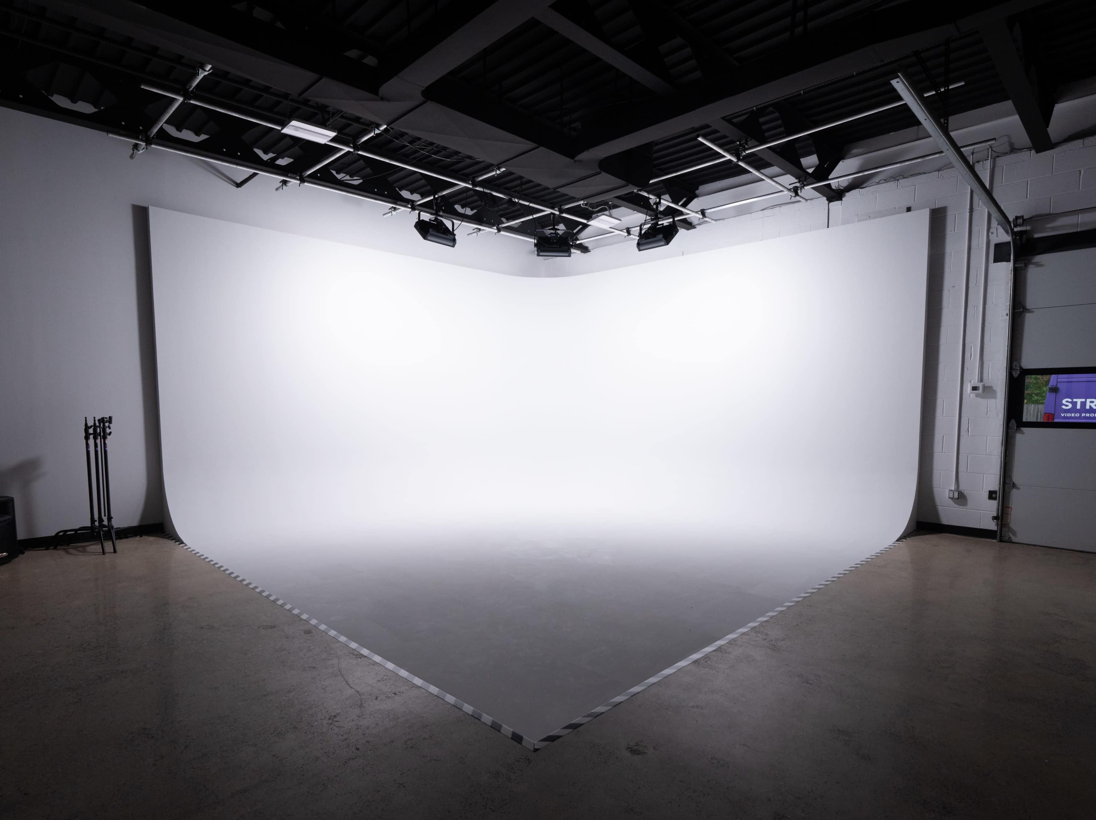 The image shows an empty, well-lit photo studio with a large white backdrop and a smooth floor.