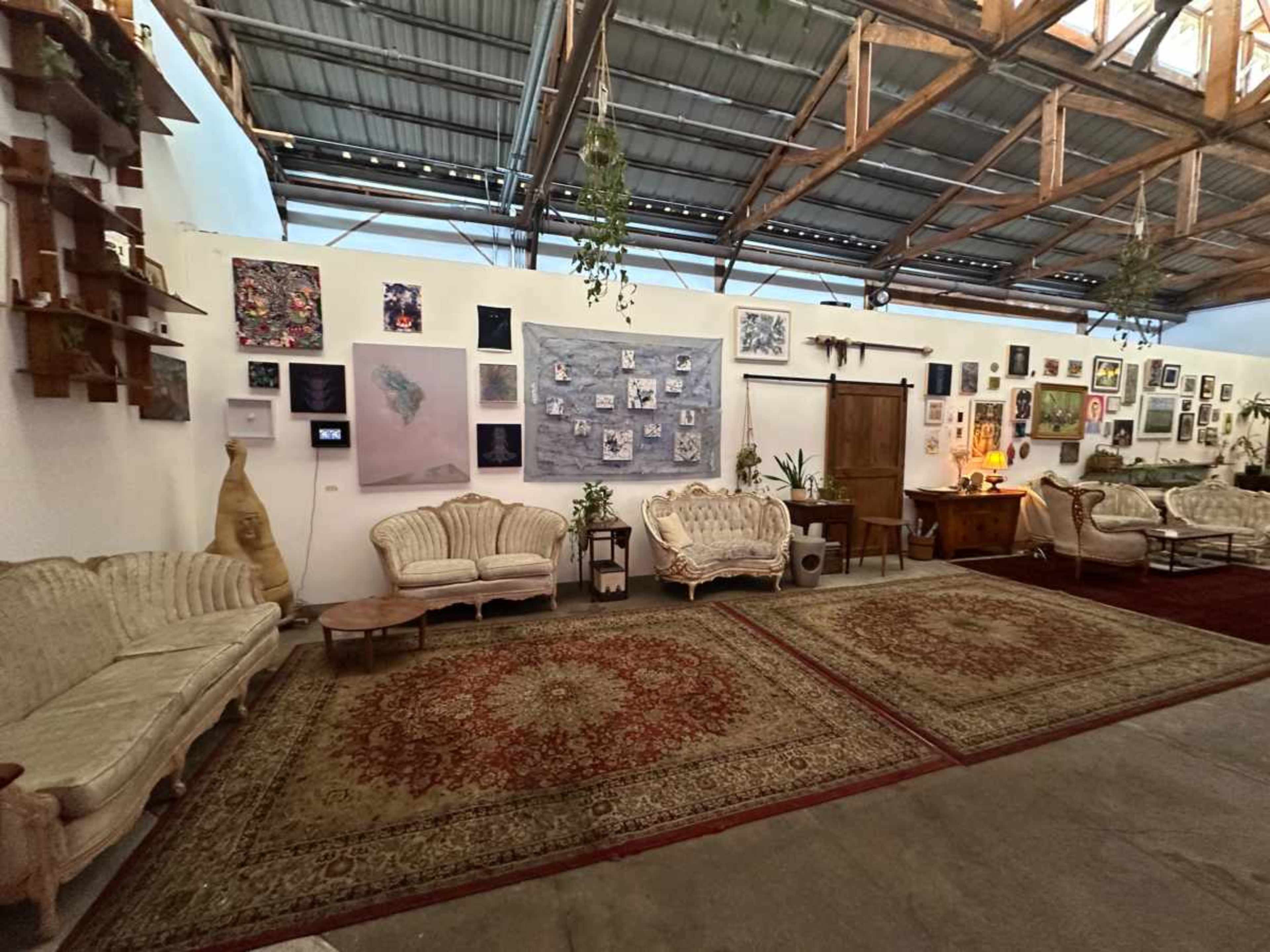 The image shows a spacious room with several vintage-style sofas, large area rugs, and a variety of wall art displayed on white walls.