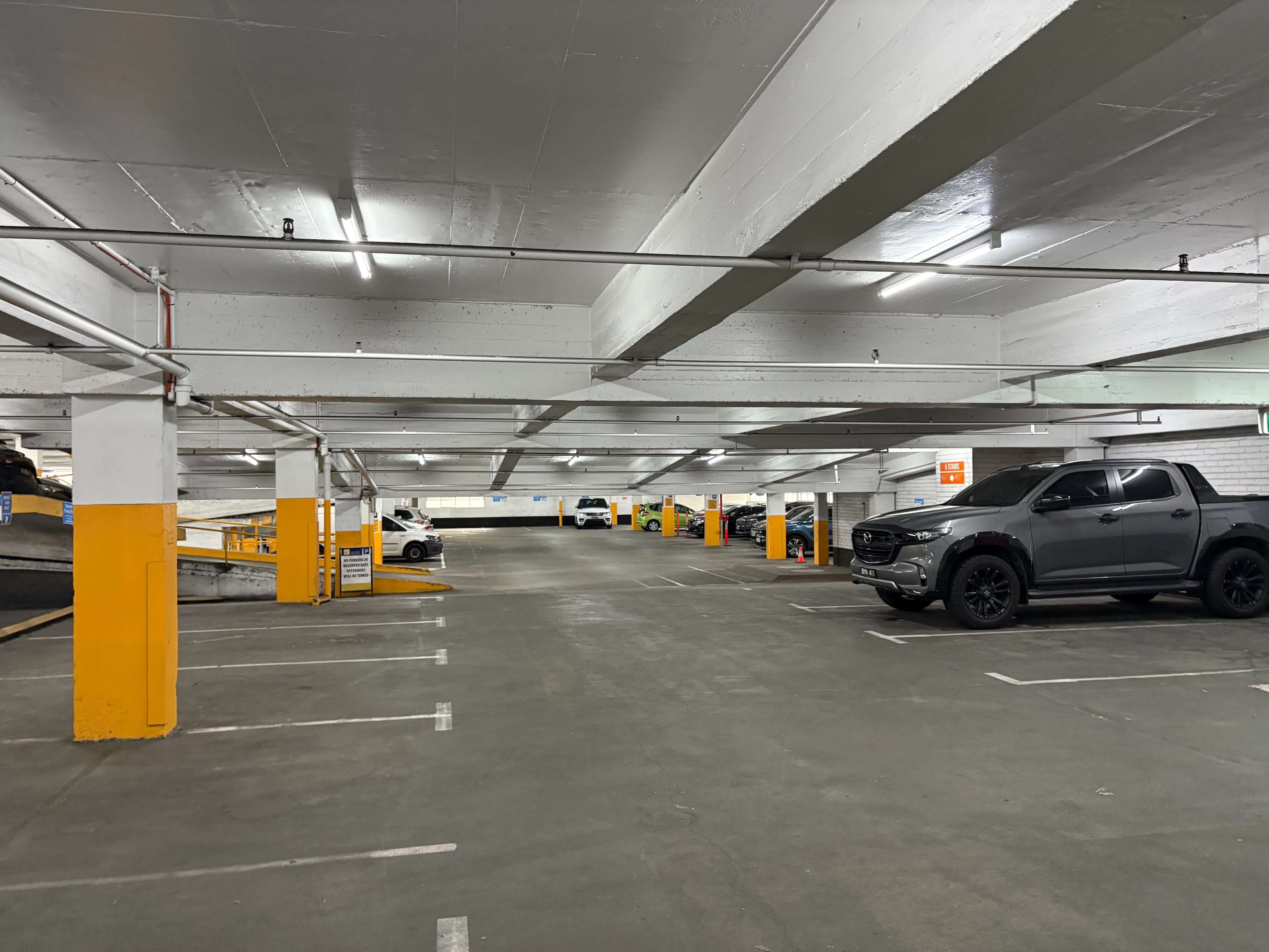 The image shows a spacious parking garage with several vehicles parked in designated spaces and yellow pillars marking the lanes.