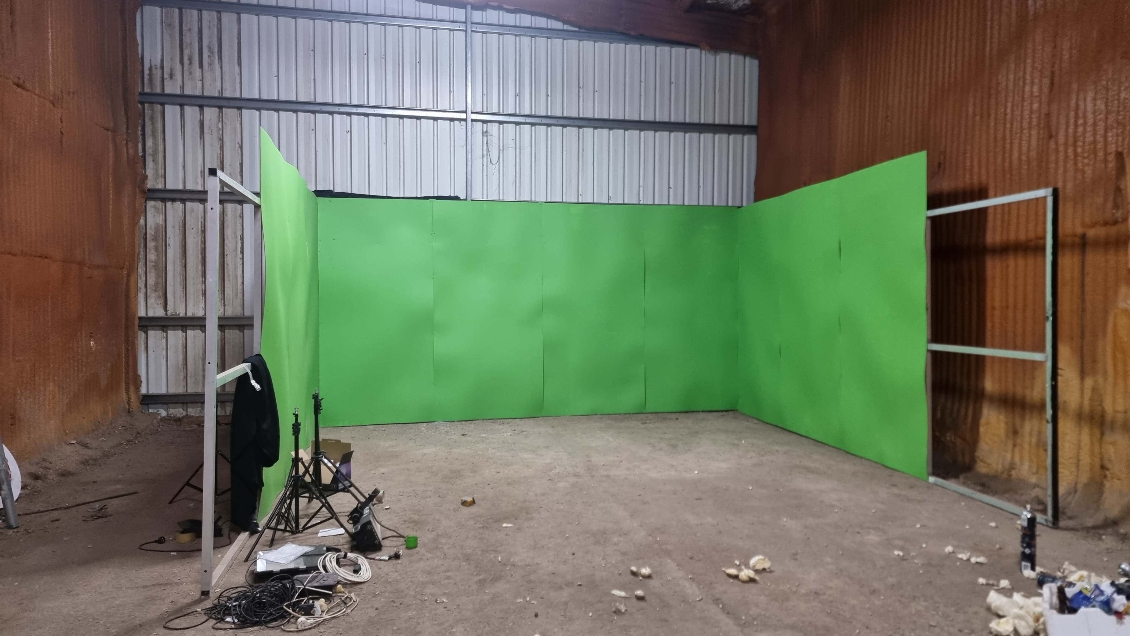 A sparse interior space with green-screen panels set up against the walls, along with some equipment and clutter on the ground.