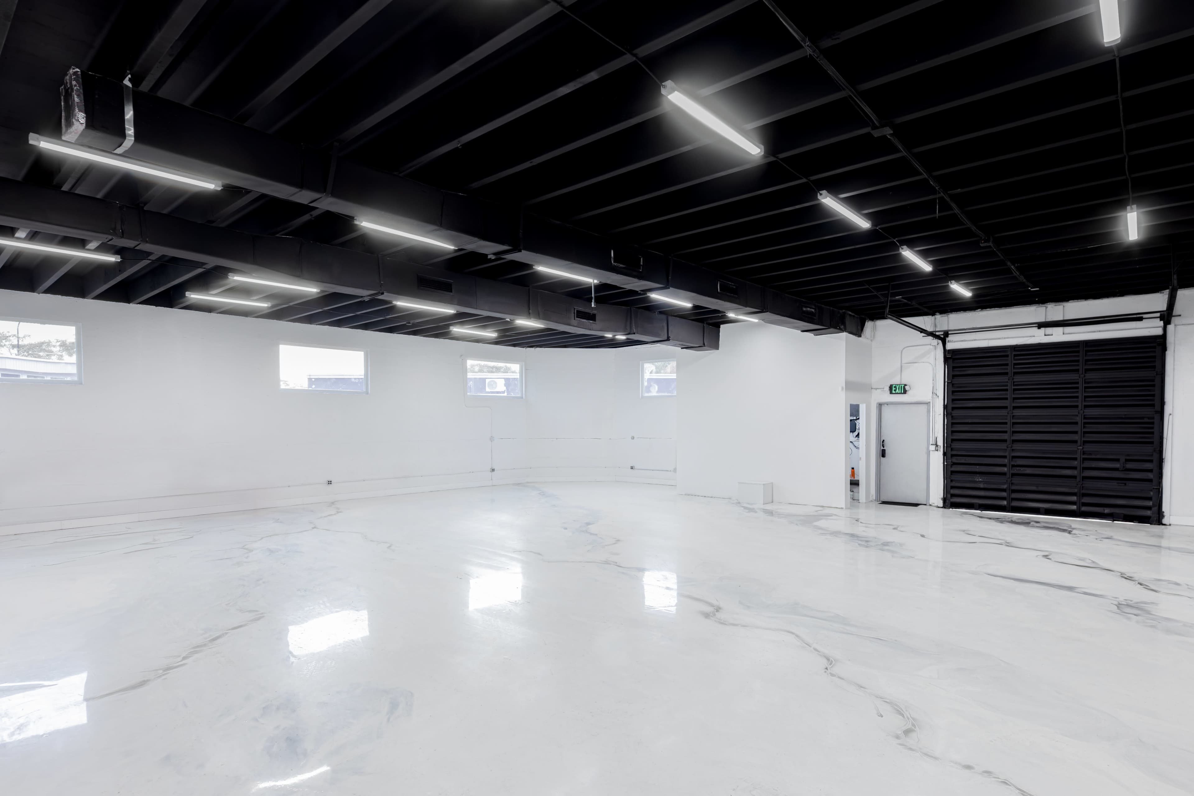 The image shows an empty indoor space with a polished marble-like floor, white walls, and black ceiling panels featuring linear light fixtures.