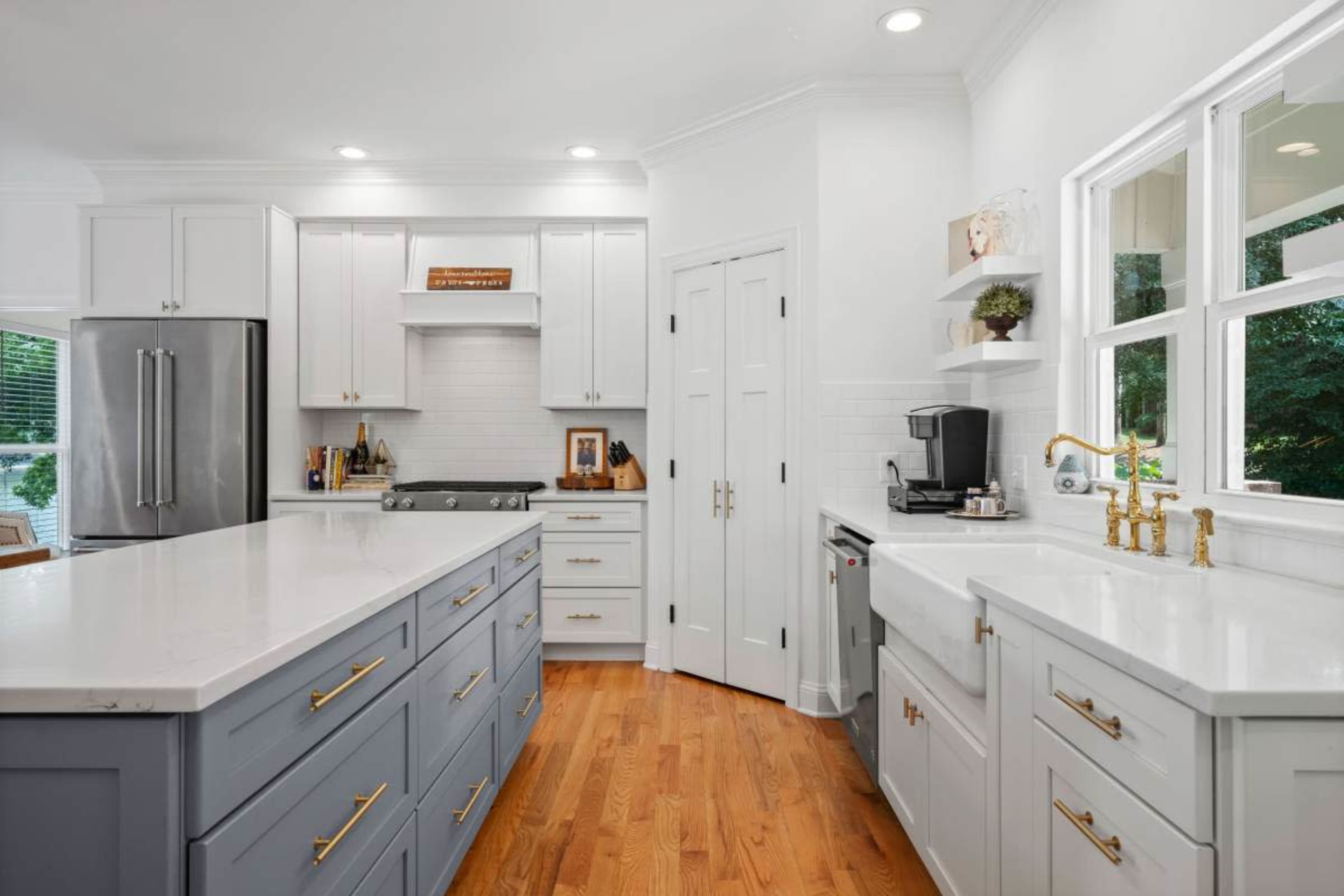 The kitchen features a central island with a gray base, white cabinets, stainless steel appliances, and a bright, open layout.