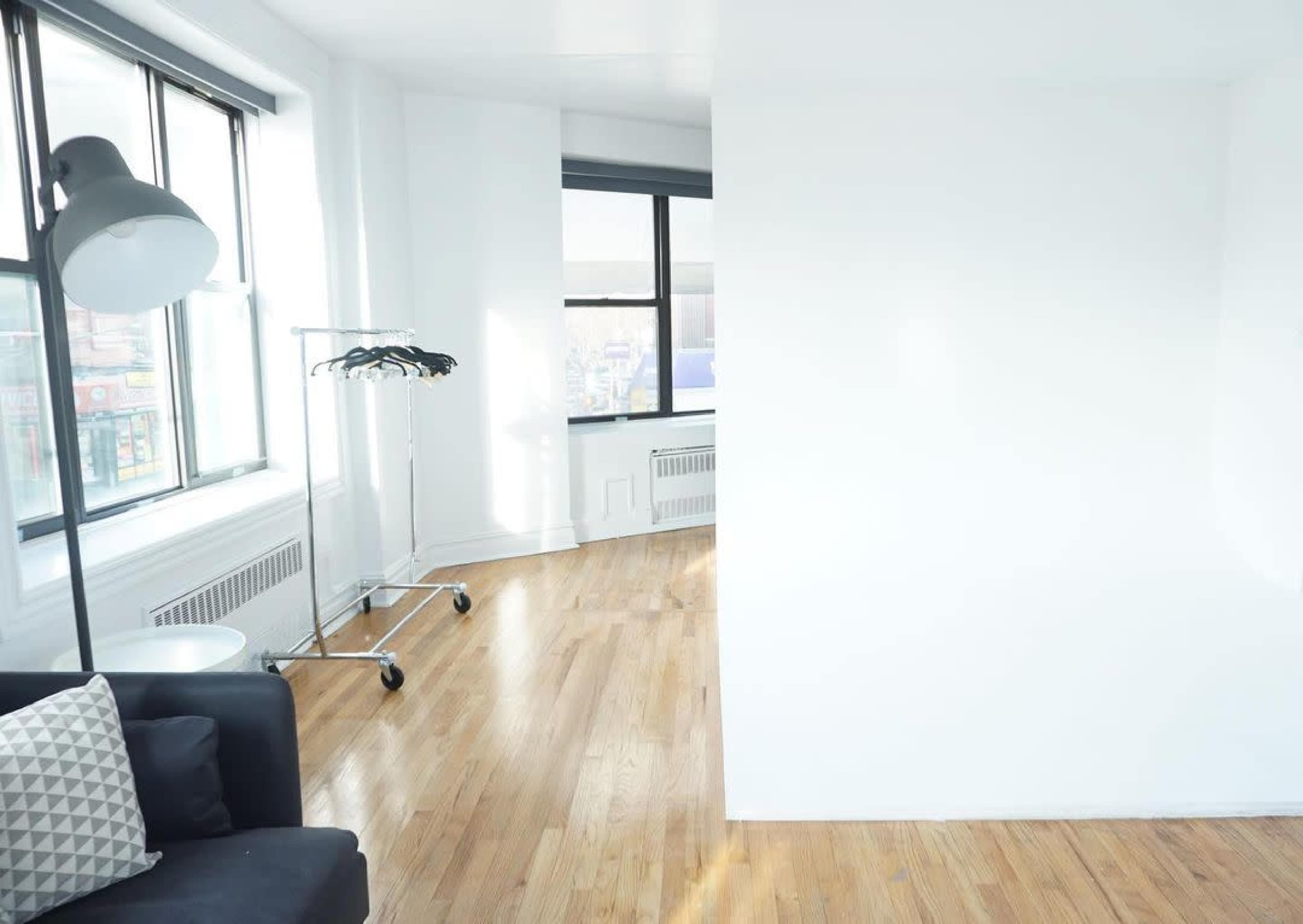 A bright, minimalist room with a black sofa, a clothing rack beside a window, and a light-colored wall.