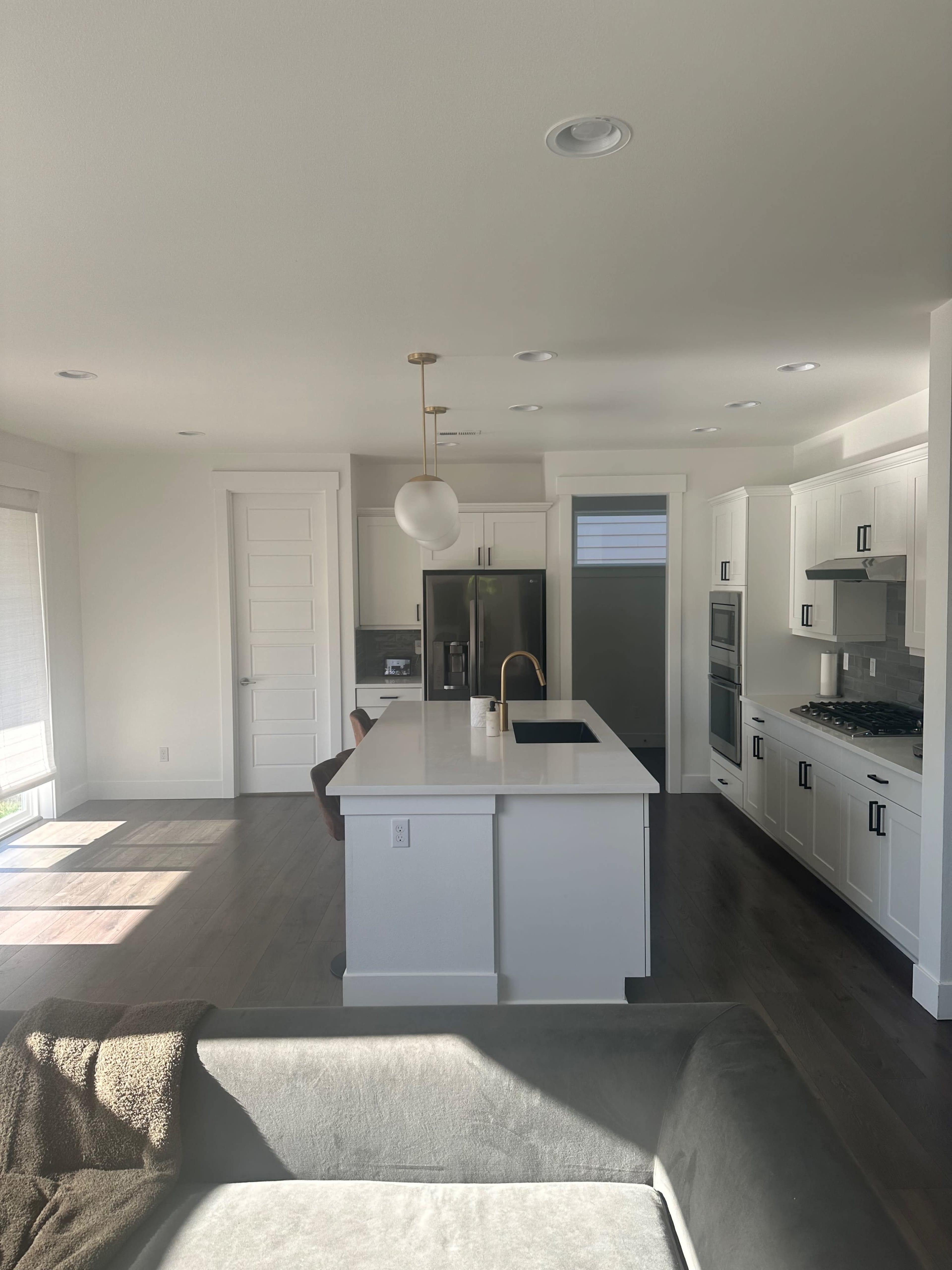 A modern kitchen features a large island with a sink, stainless steel appliances, and white cabinetry, illuminated by a pendant light.