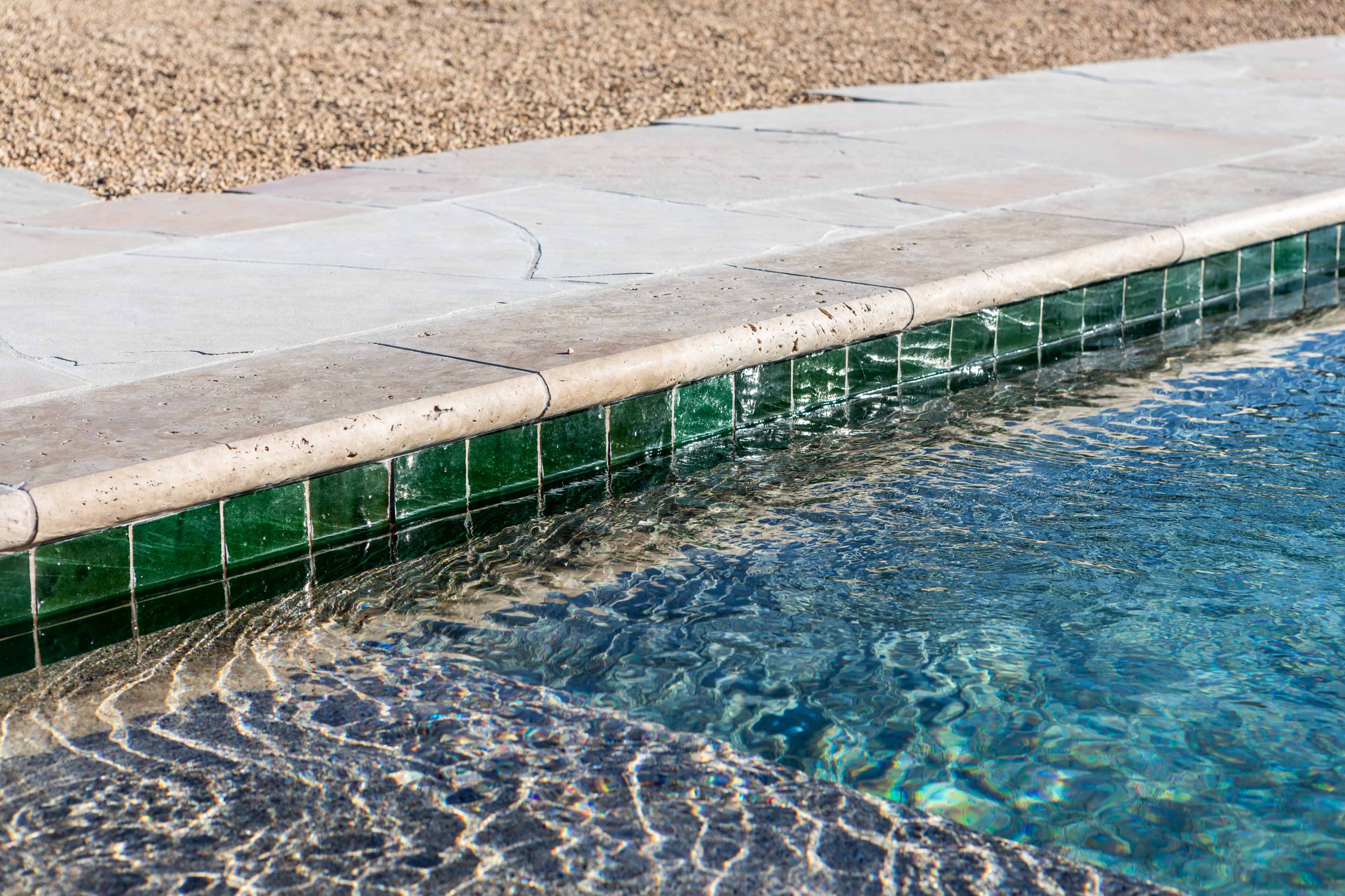 The image shows a close-up of a pool's edge, featuring a tiled border and rippling water.