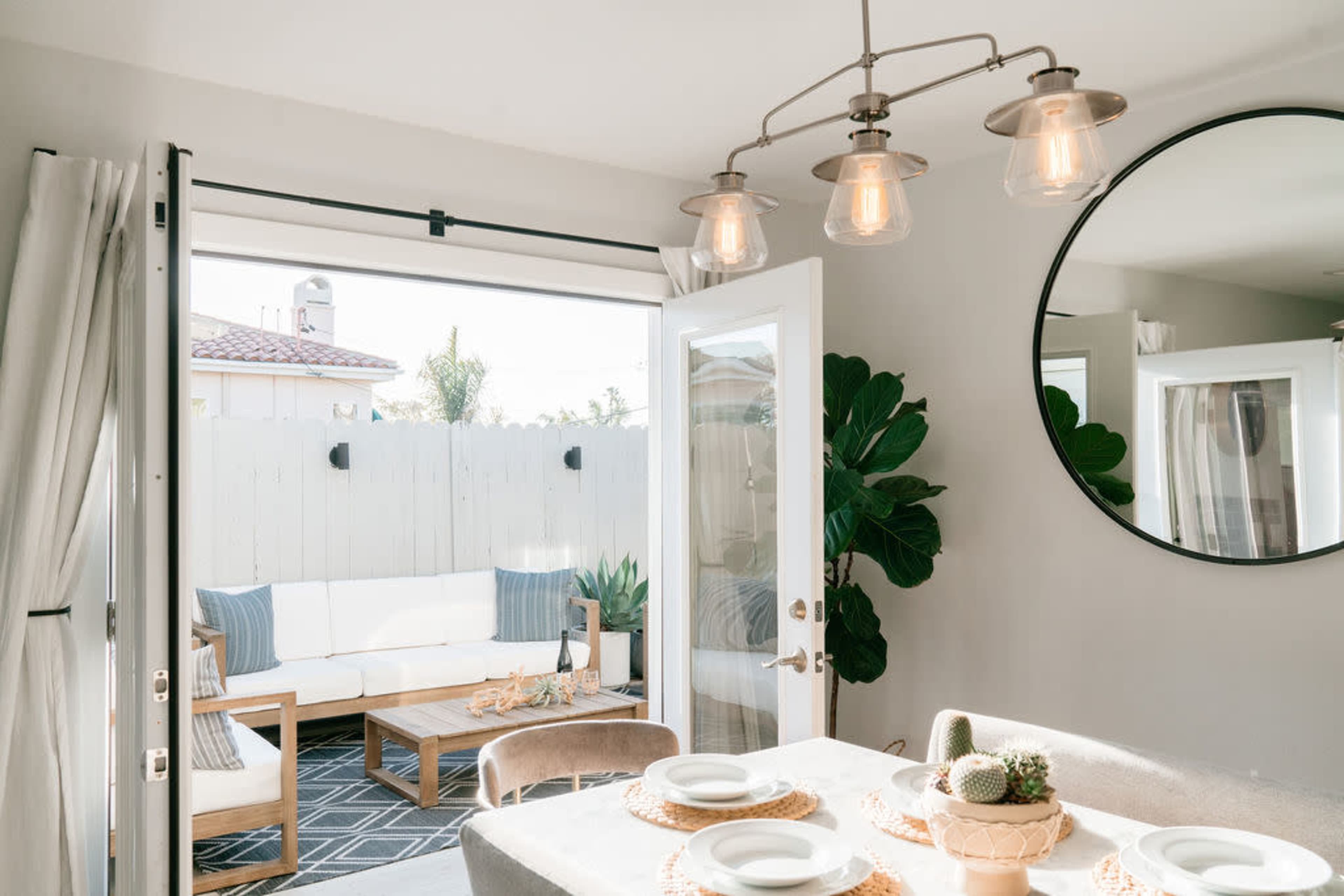 A dining area features a table set with plates and a centerpiece, alongside an open door leading to a patio with outdoor seating.