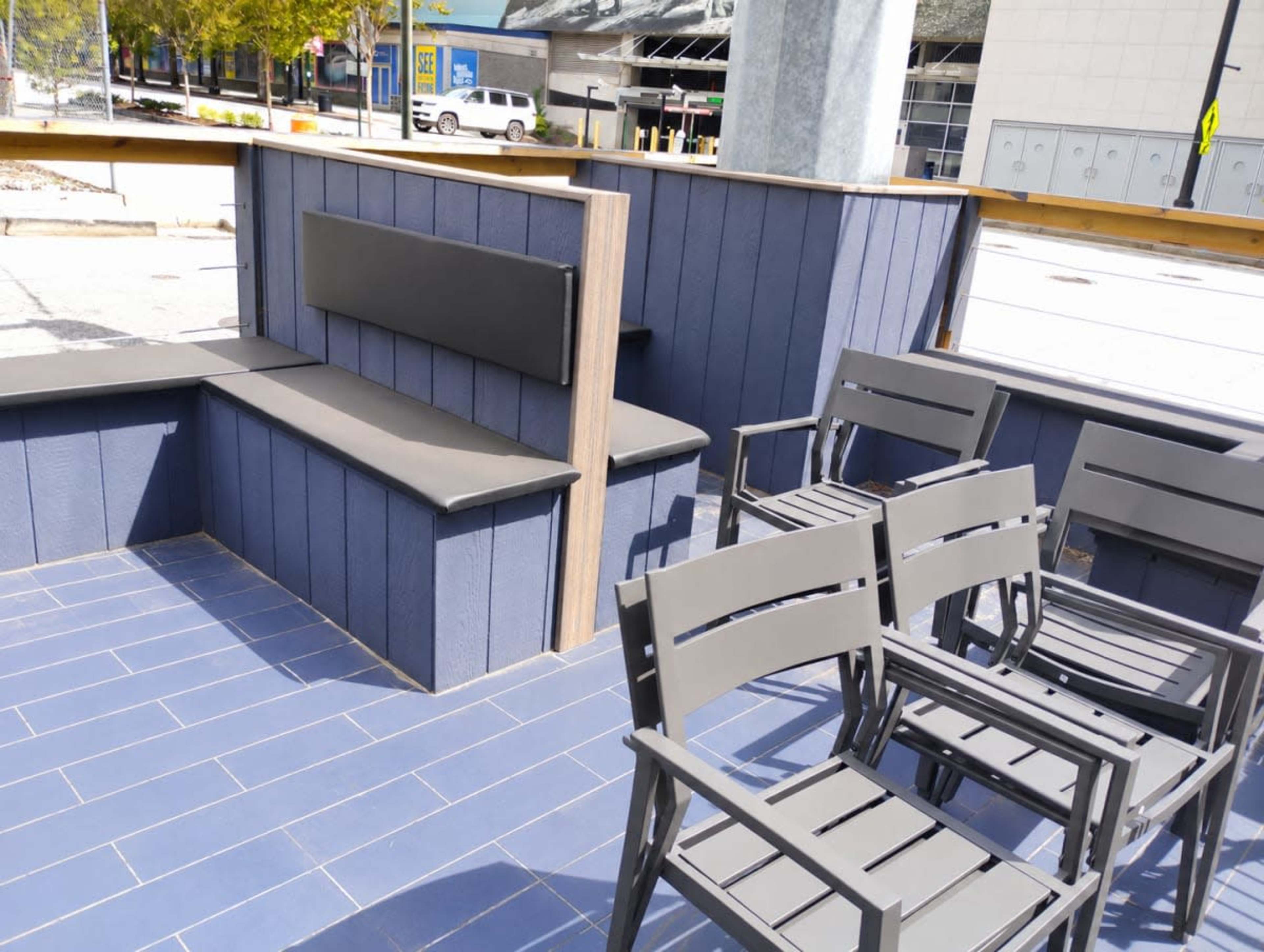 The image shows a modern seating area with a built-in bench and metal chairs arranged around a tiled floor in an outdoor setting.