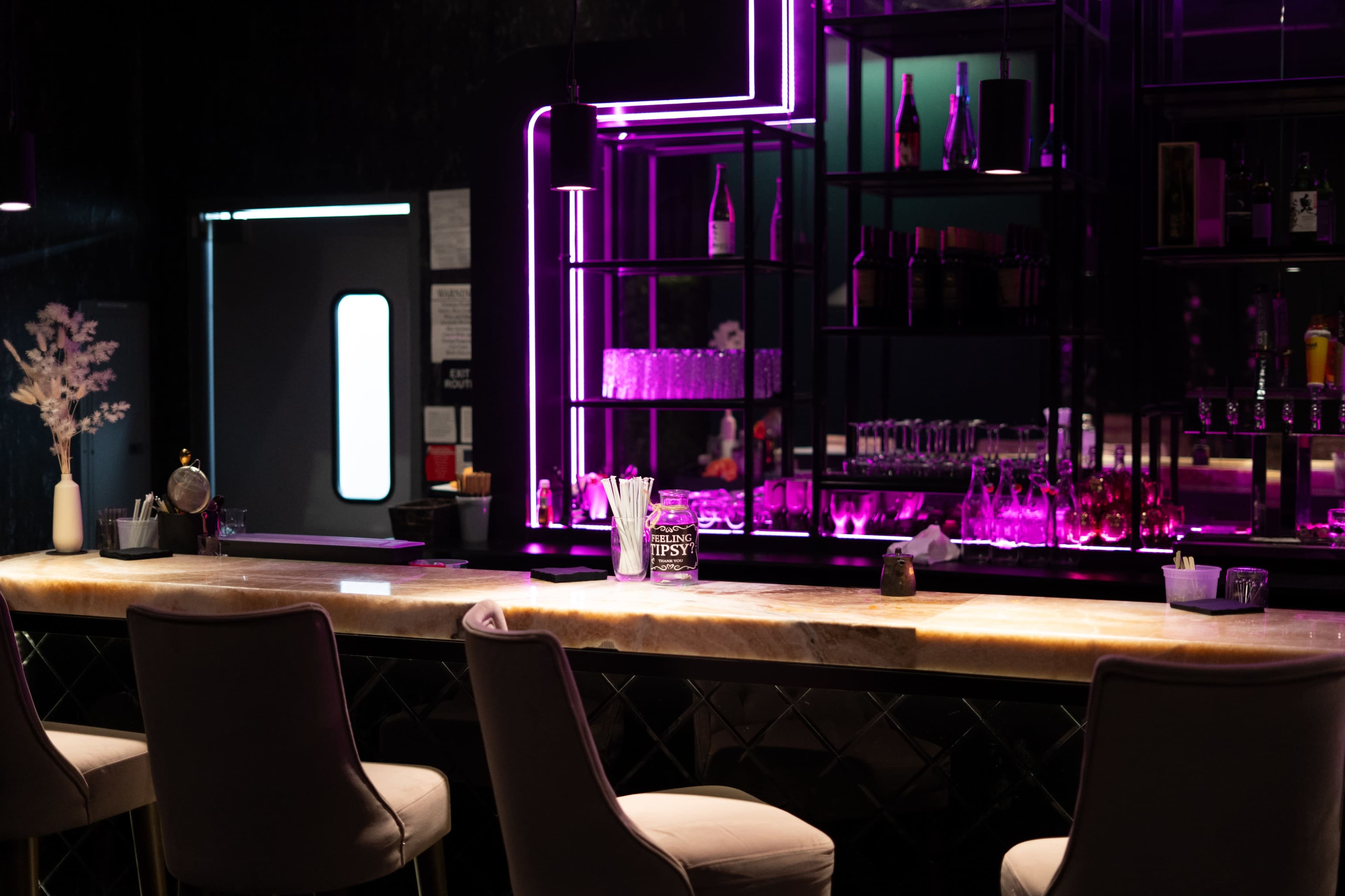 A modern bar featuring a sleek countertop, illuminated shelves, and vibrant neon lighting.