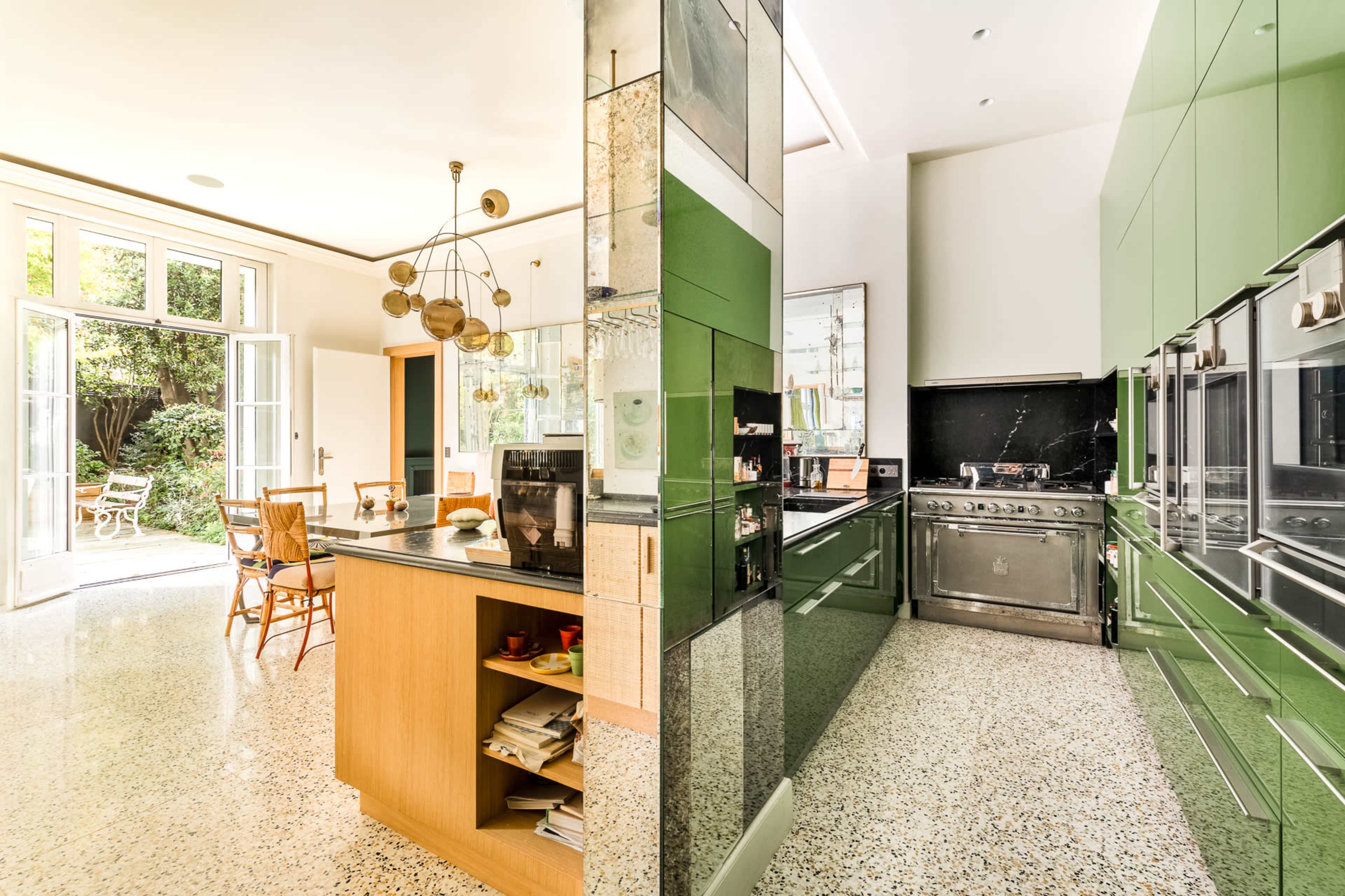 A modern kitchen with green cabinetry, a stainless steel stove, and a dining area that opens to a backyard patio.
