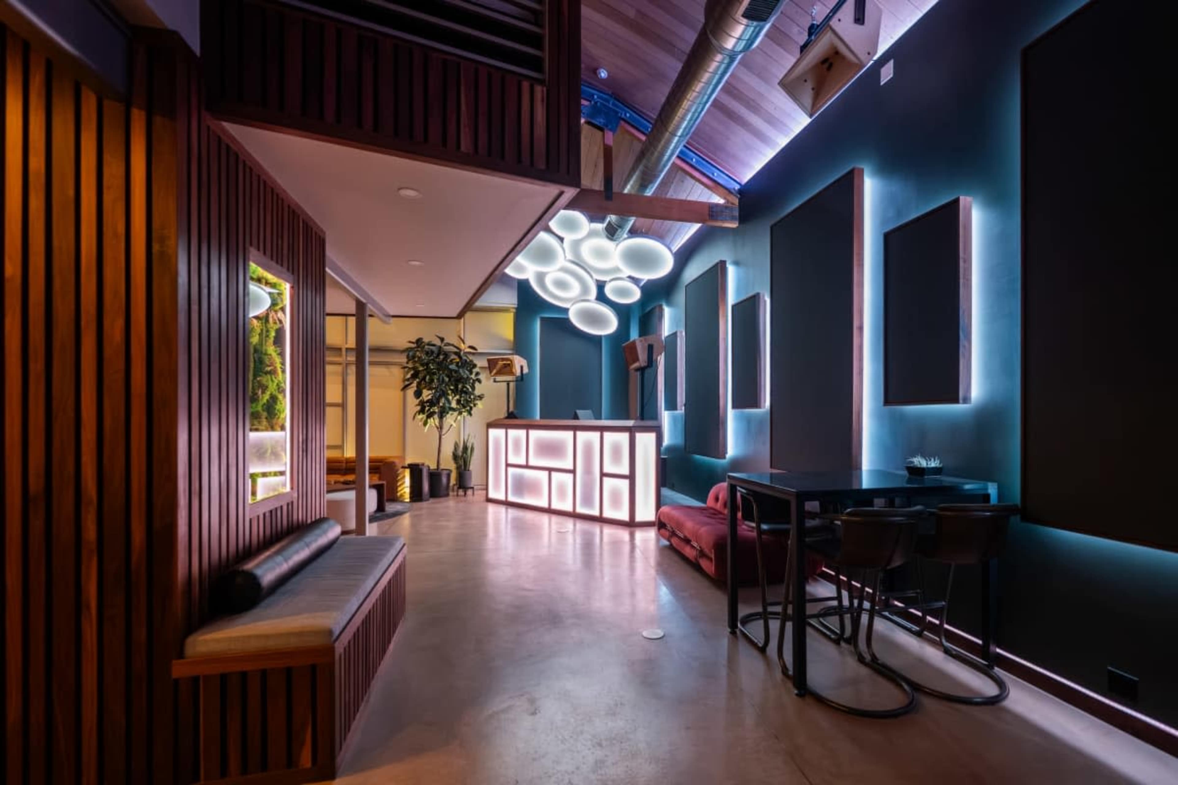 The image shows a modern interior space with wooden paneling, a glowing bar area, and stylish lighting fixtures.