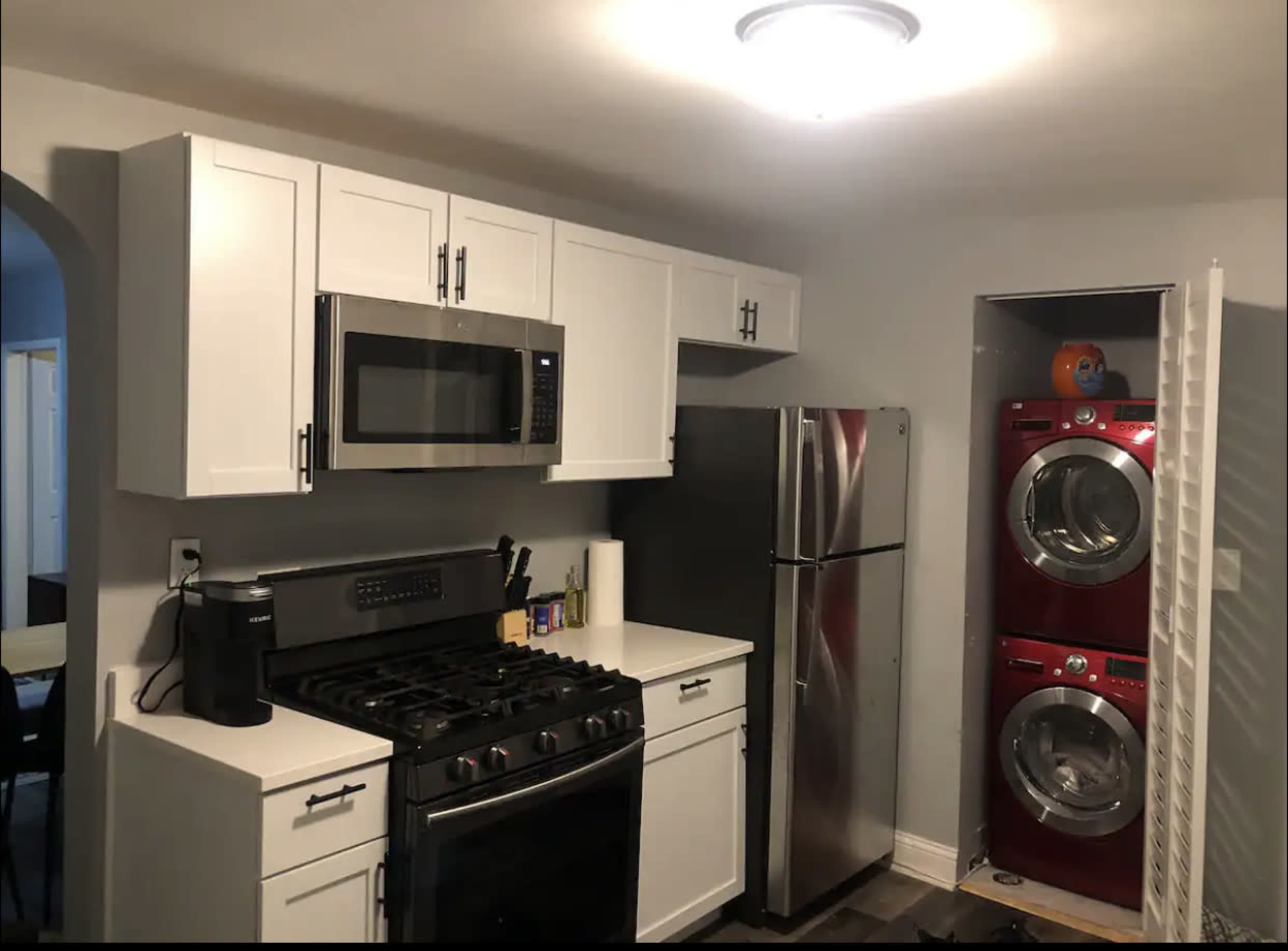 The kitchen features white cabinetry, a stainless steel refrigerator, a gas stove, and a stacked washer and dryer in red.