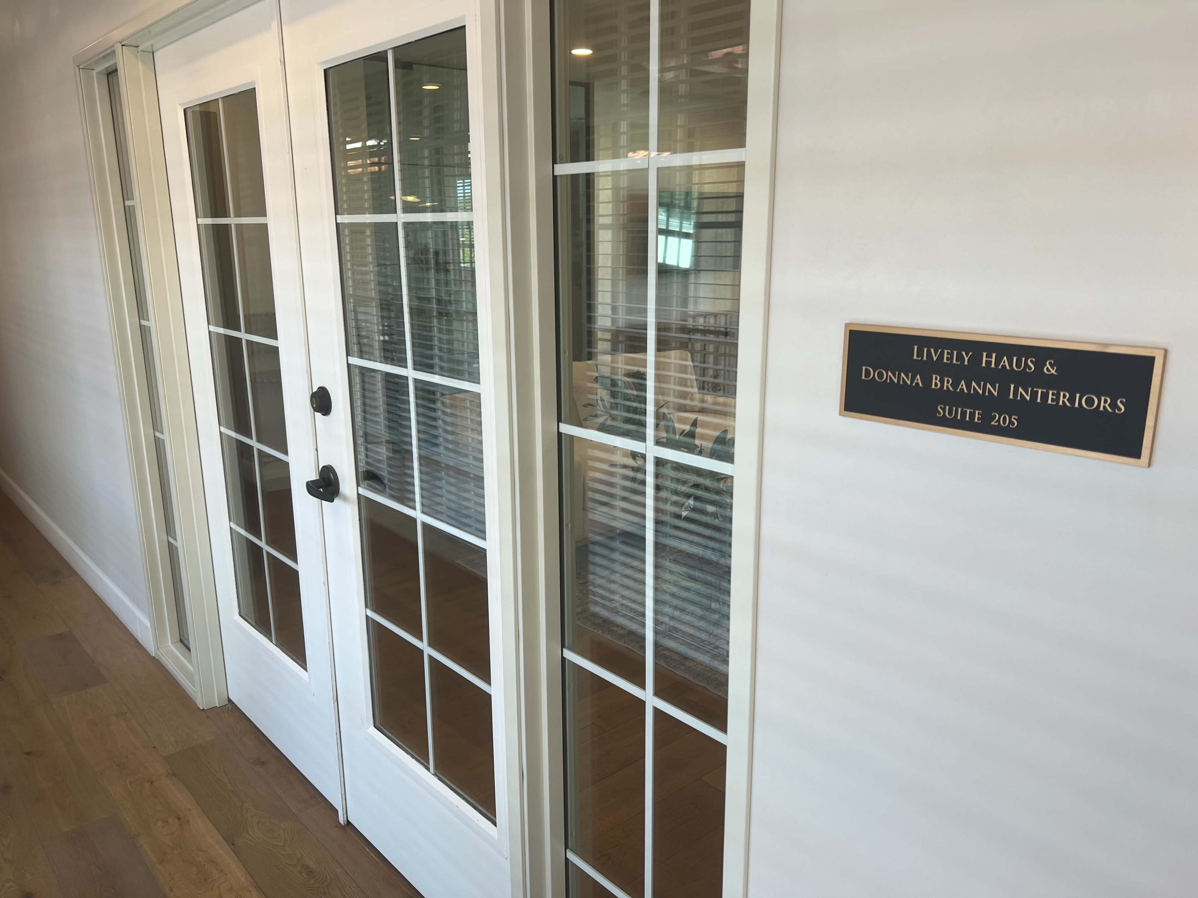 A set of double glass doors with a plaque next to them indicating "Lively Haus & Donna Brann Interiors, Suite 205."