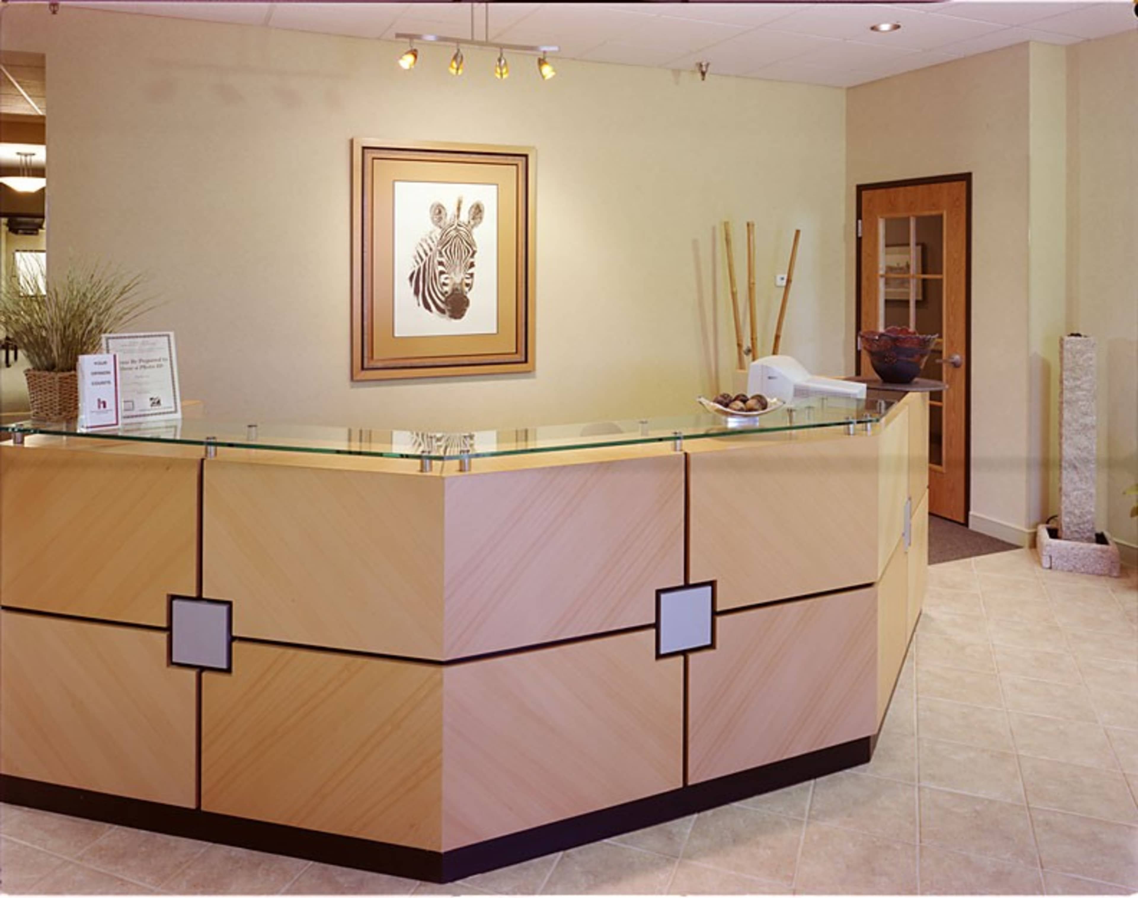 A reception area with a wooden front desk, a zebra artwork on the wall, and potted plants in the corner.