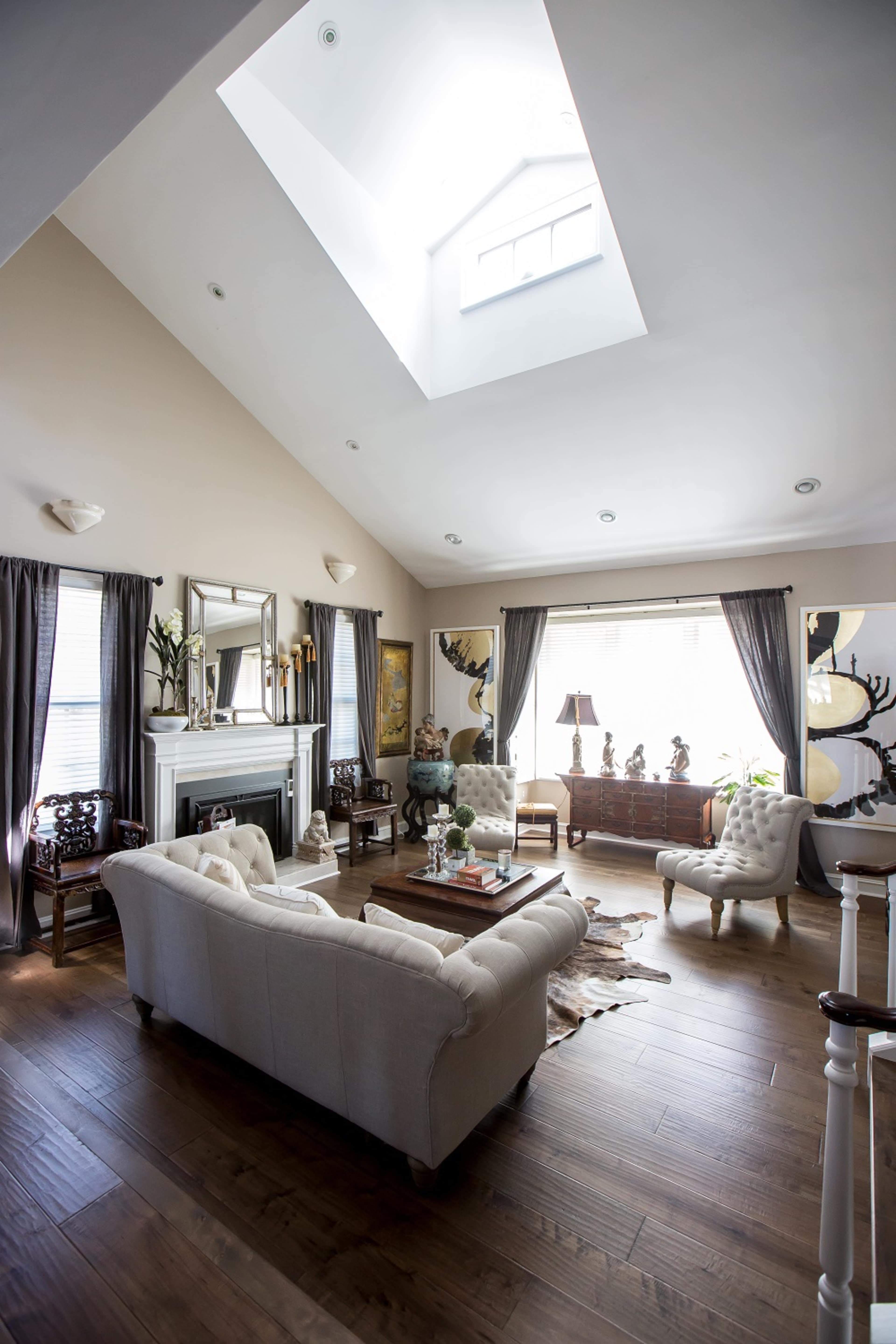 The living room features a skylight above a light-colored sofa, dark curtains, and wooden flooring, with a fireplace and decorative furniture.