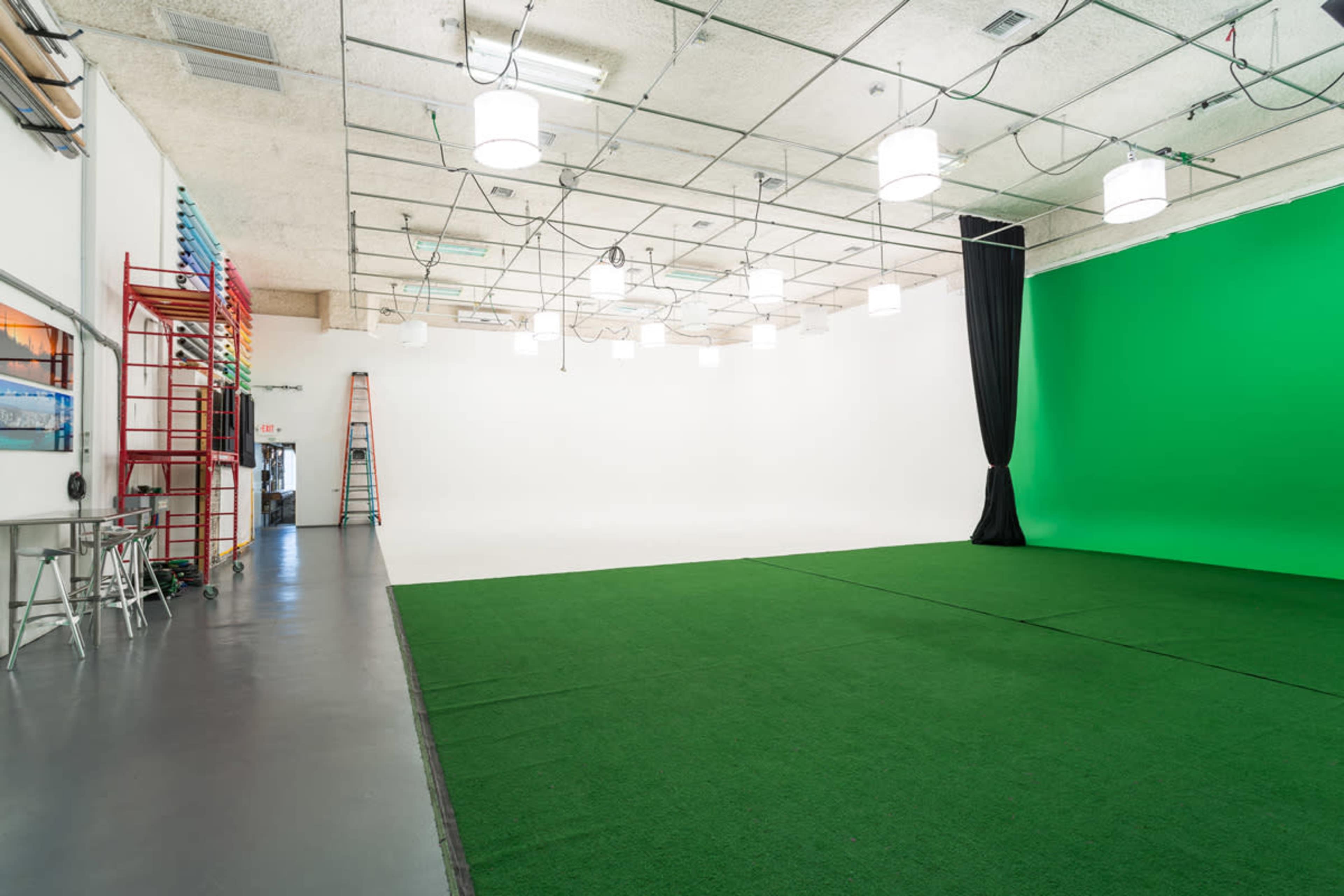 A spacious studio with a green screen wall, artificial lighting, and a carpeted floor.