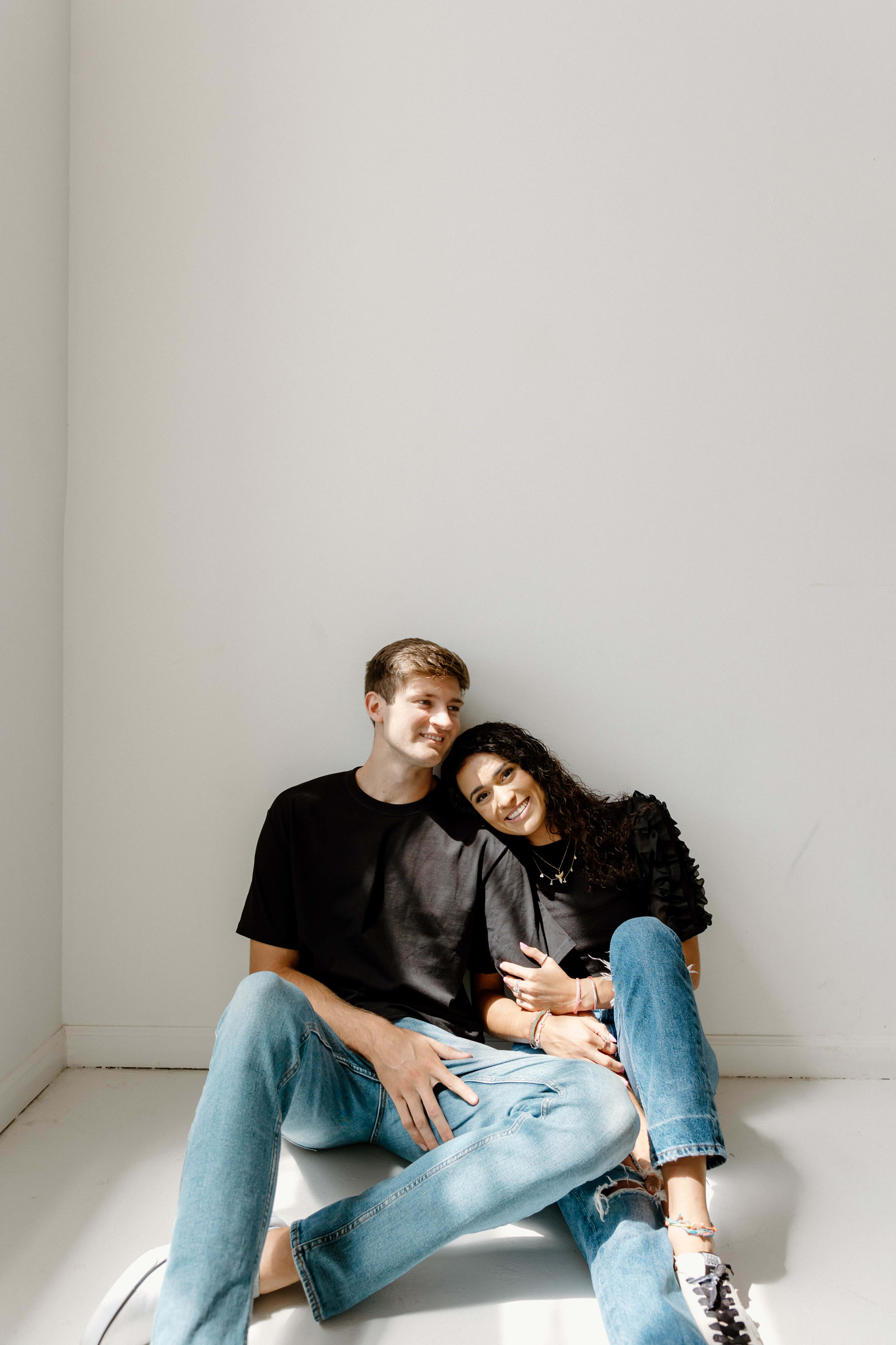 A couple ins black posing for a photoshoot, sitting on the floor.