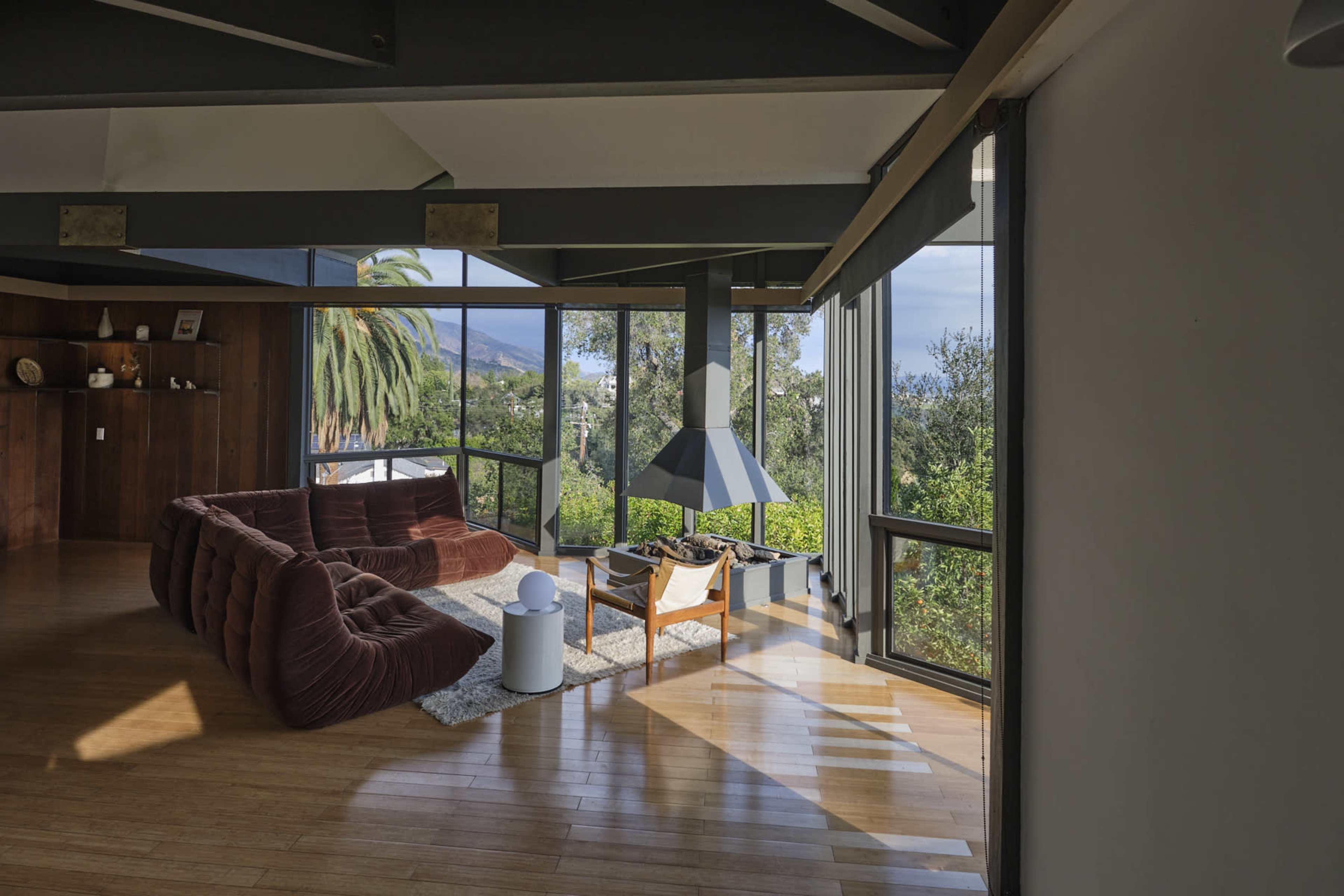 A modern living room features a large sectional sofa, a floor lamp, and expansive windows that overlook greenery and a distant landscape.
