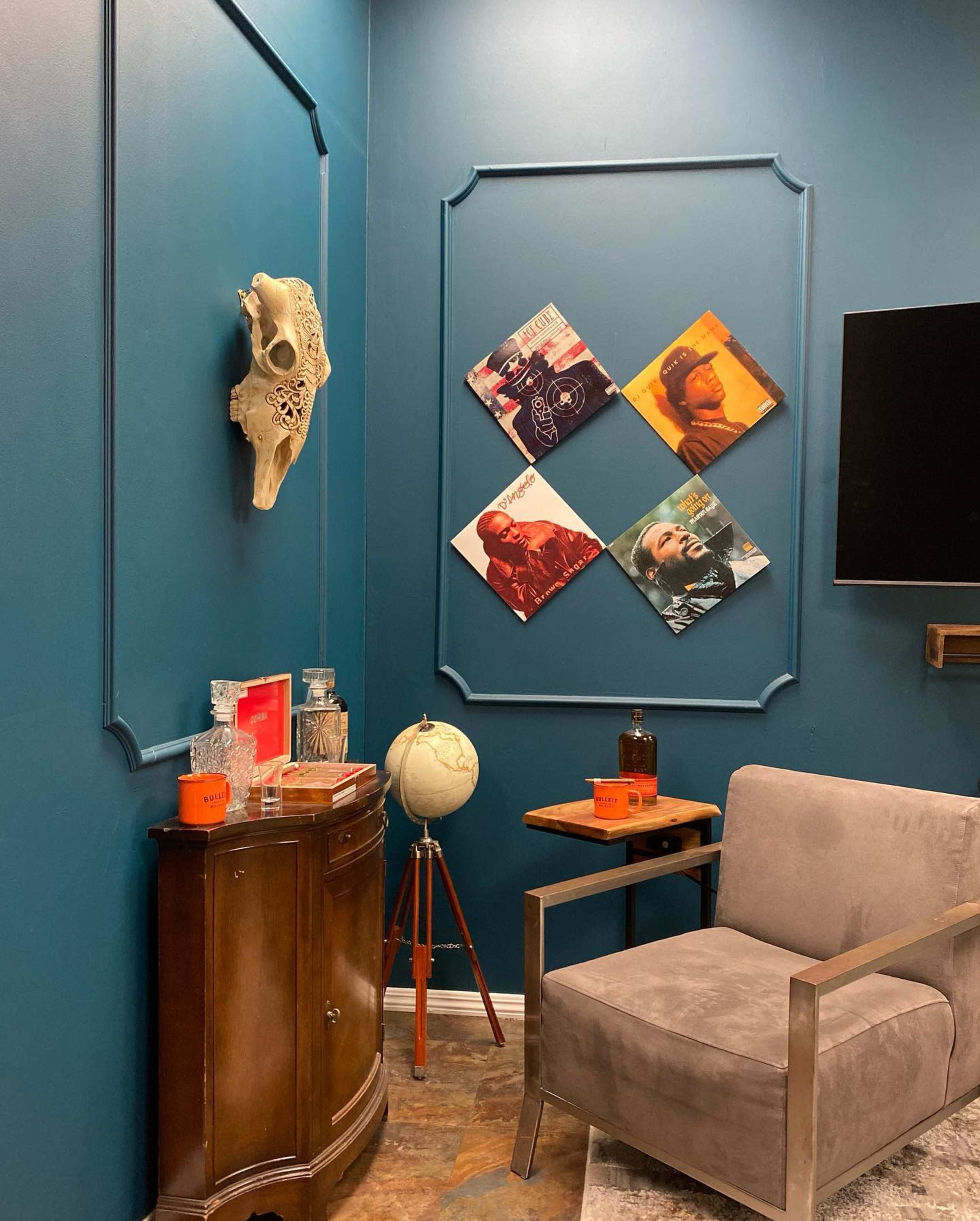 A cozy corner with a gray chair, a wooden side table, a globe on a stand, and four framed photos arranged on a teal wall, alongside a decorative skull.