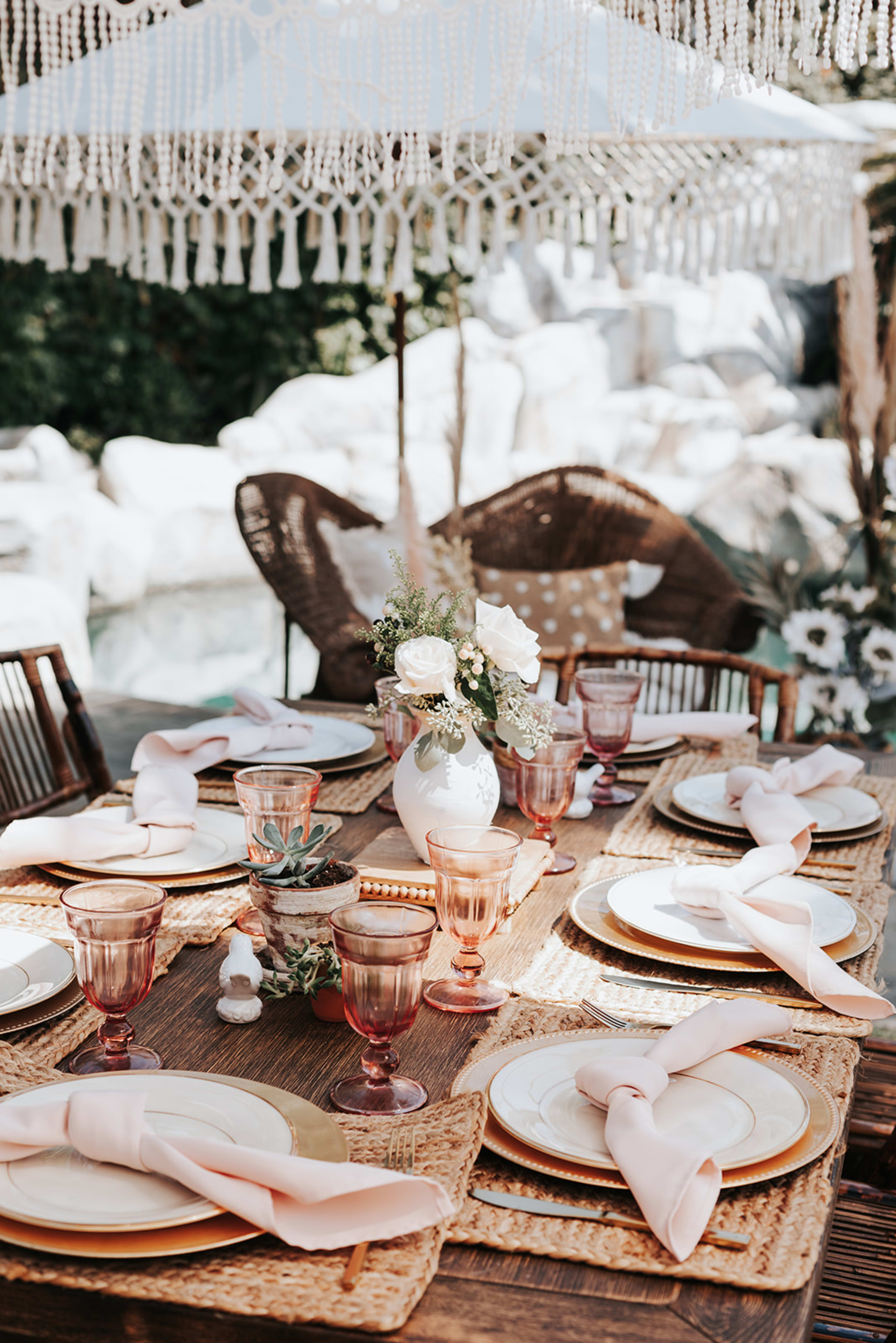 Ein im Boho-Stil gedeckter Tisch im Freien mit weißen Tellern und Gläsern.