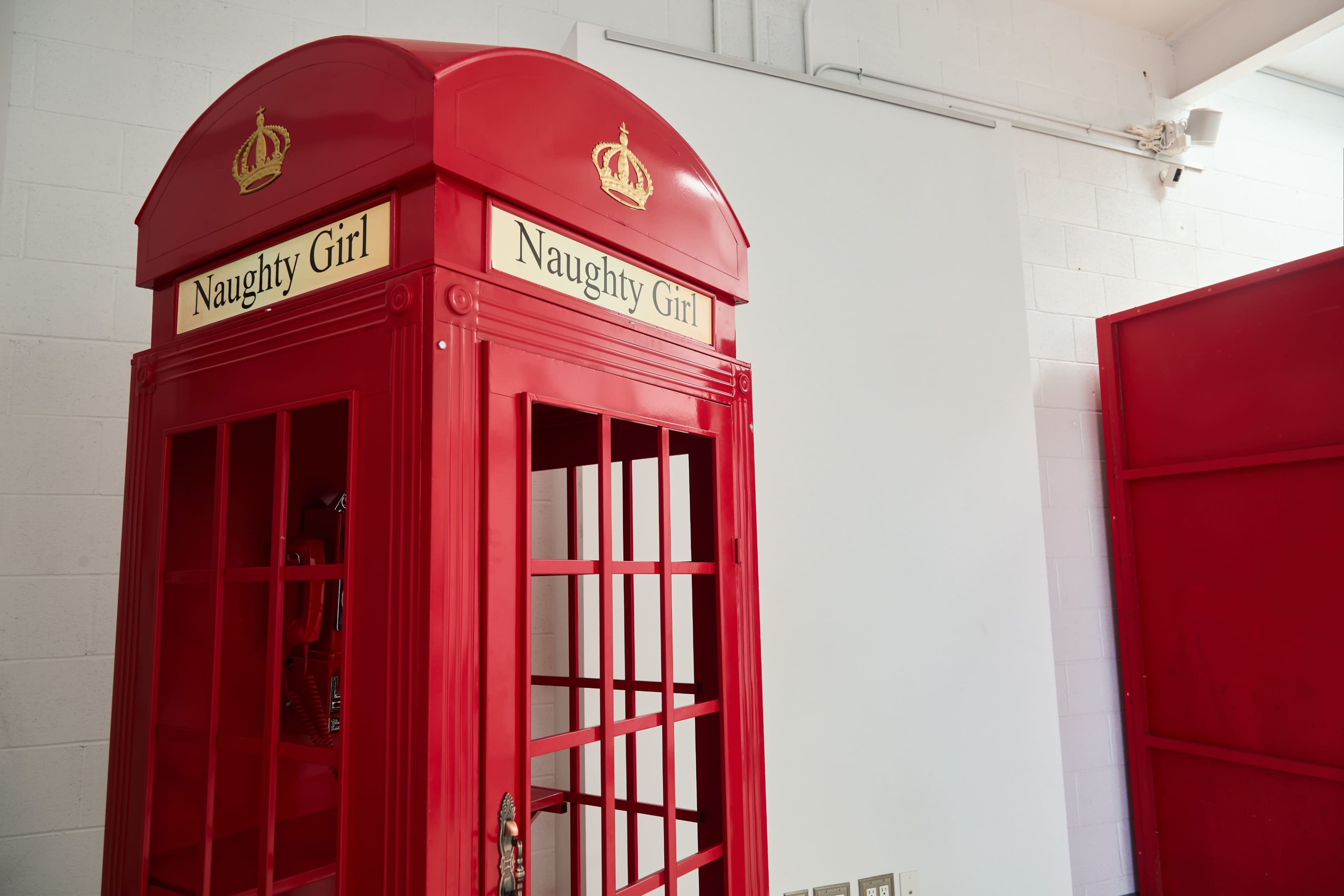 The image shows a red telephone box with the words "Naughty Girl" displayed on its top sign, set against a white background.
