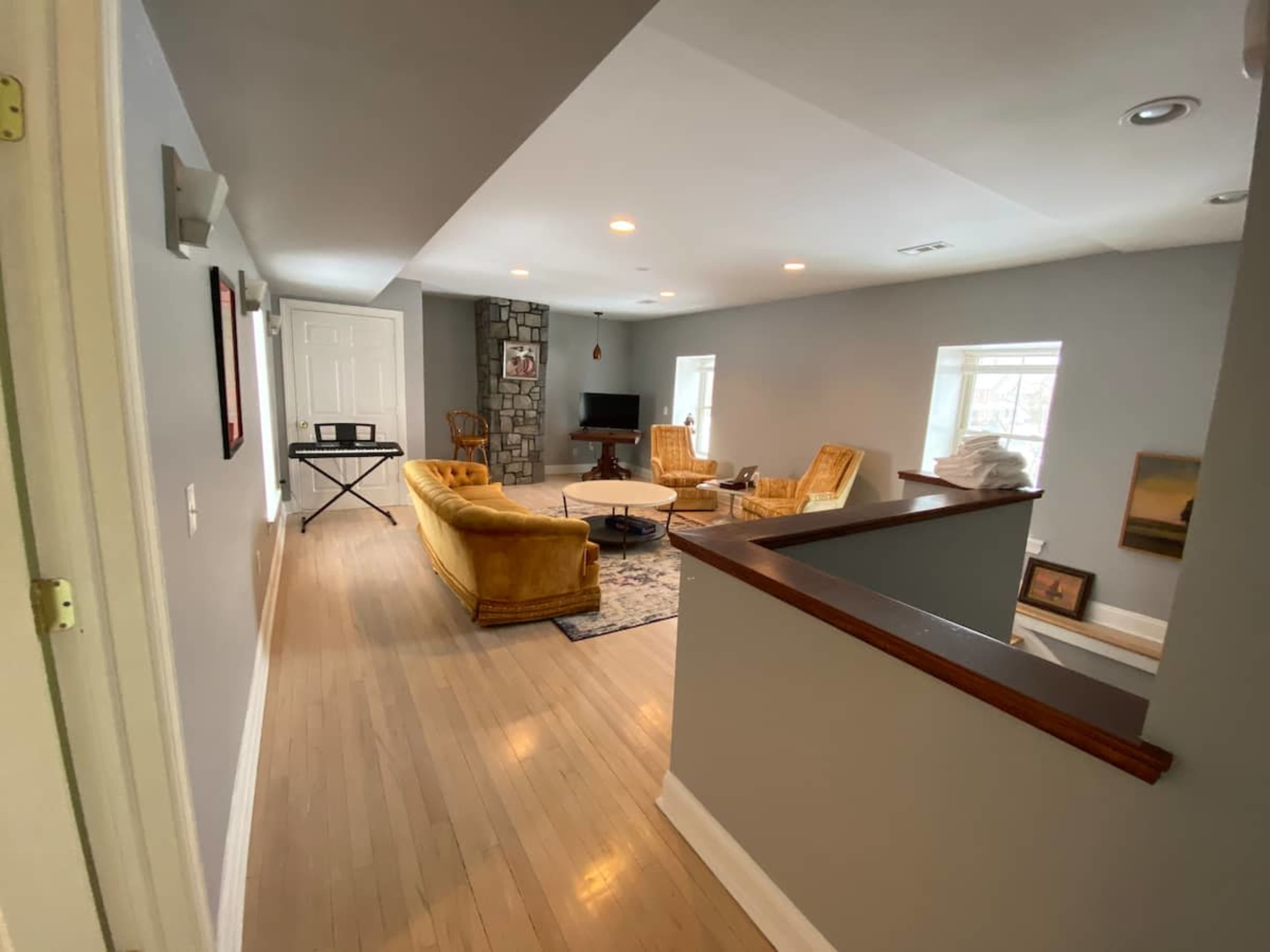 A hallway leads to a spacious living area featuring a yellow couch, two armchairs, and a stone fireplace.