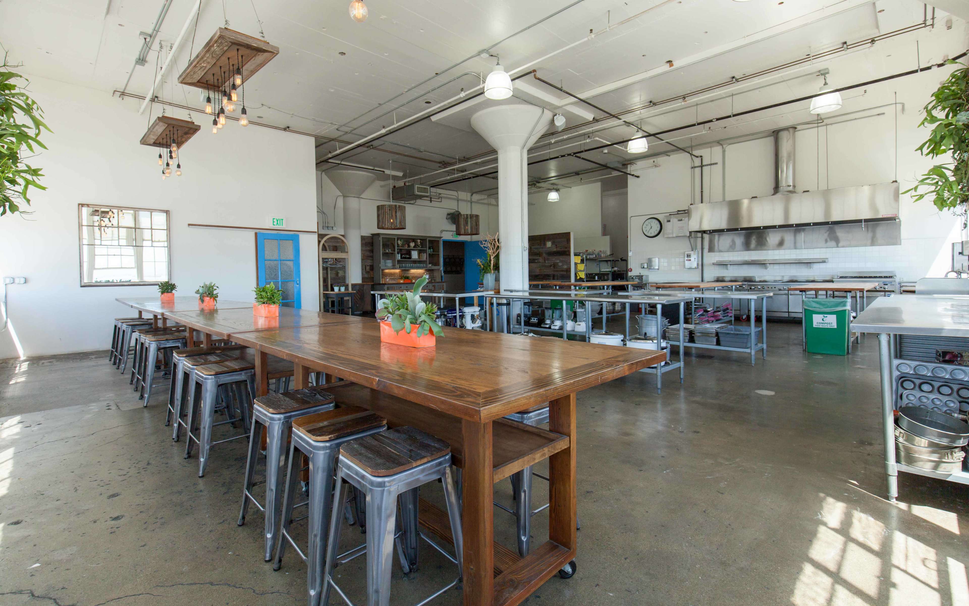 A spacious kitchen and dining area with a long wooden table, metal stools, and stainless steel appliances.