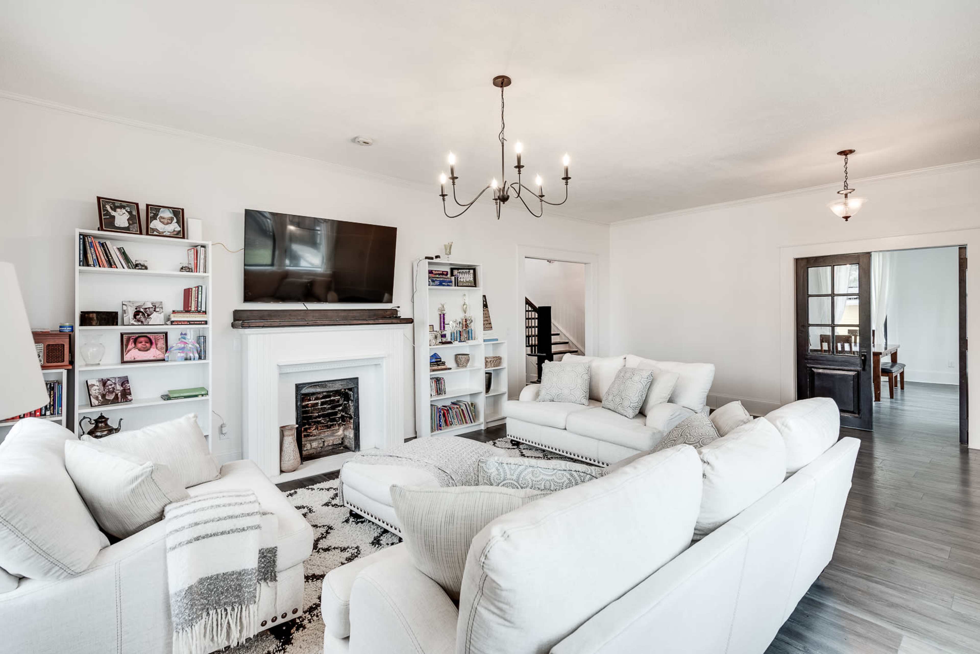 The living room features a white sectional sofa, a fireplace, a television mounted on the wall, and bookshelves filled with books and family photos.