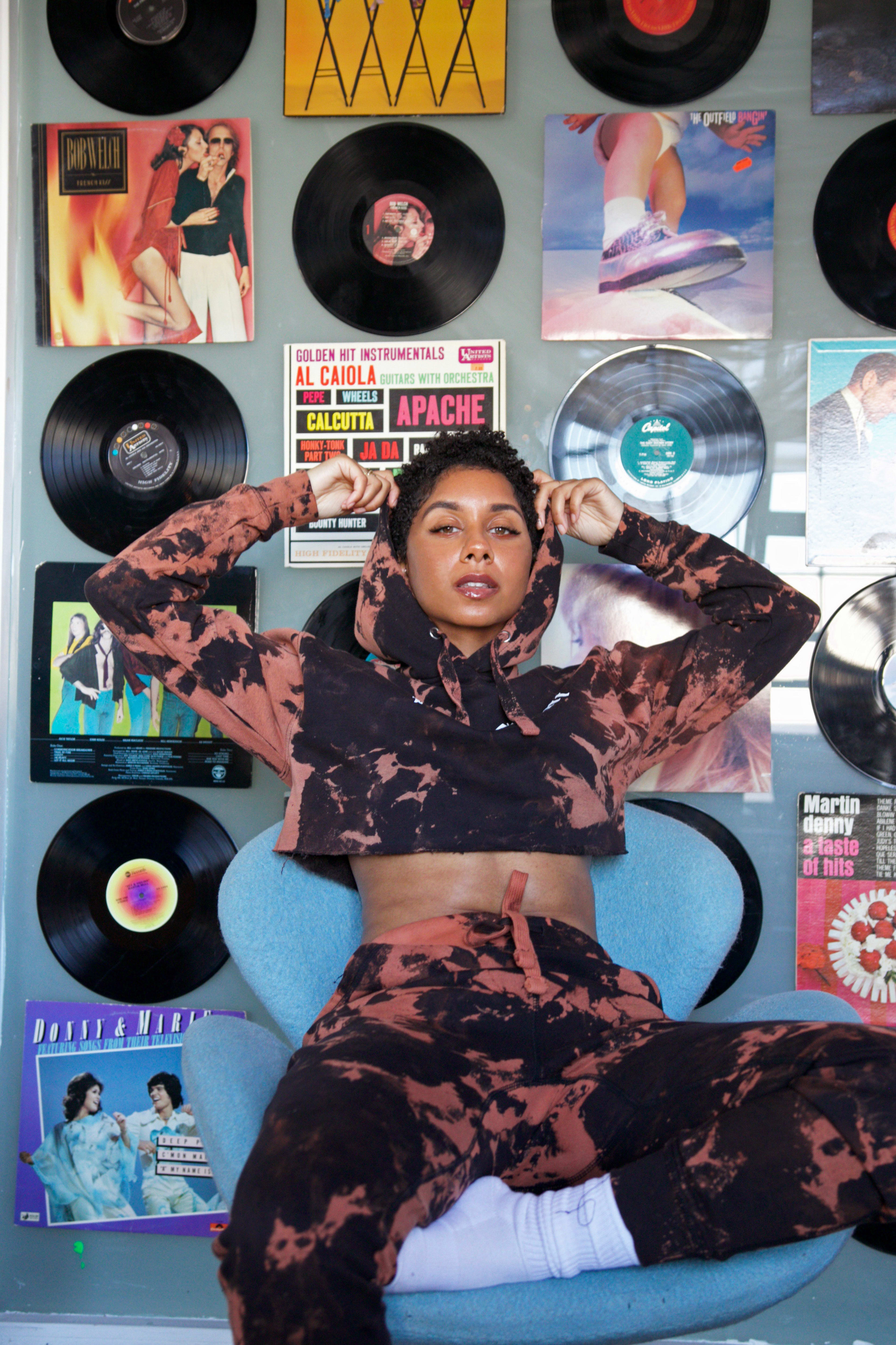 A retro photo shoot of a woman posing on a chair in front of a wall of records.