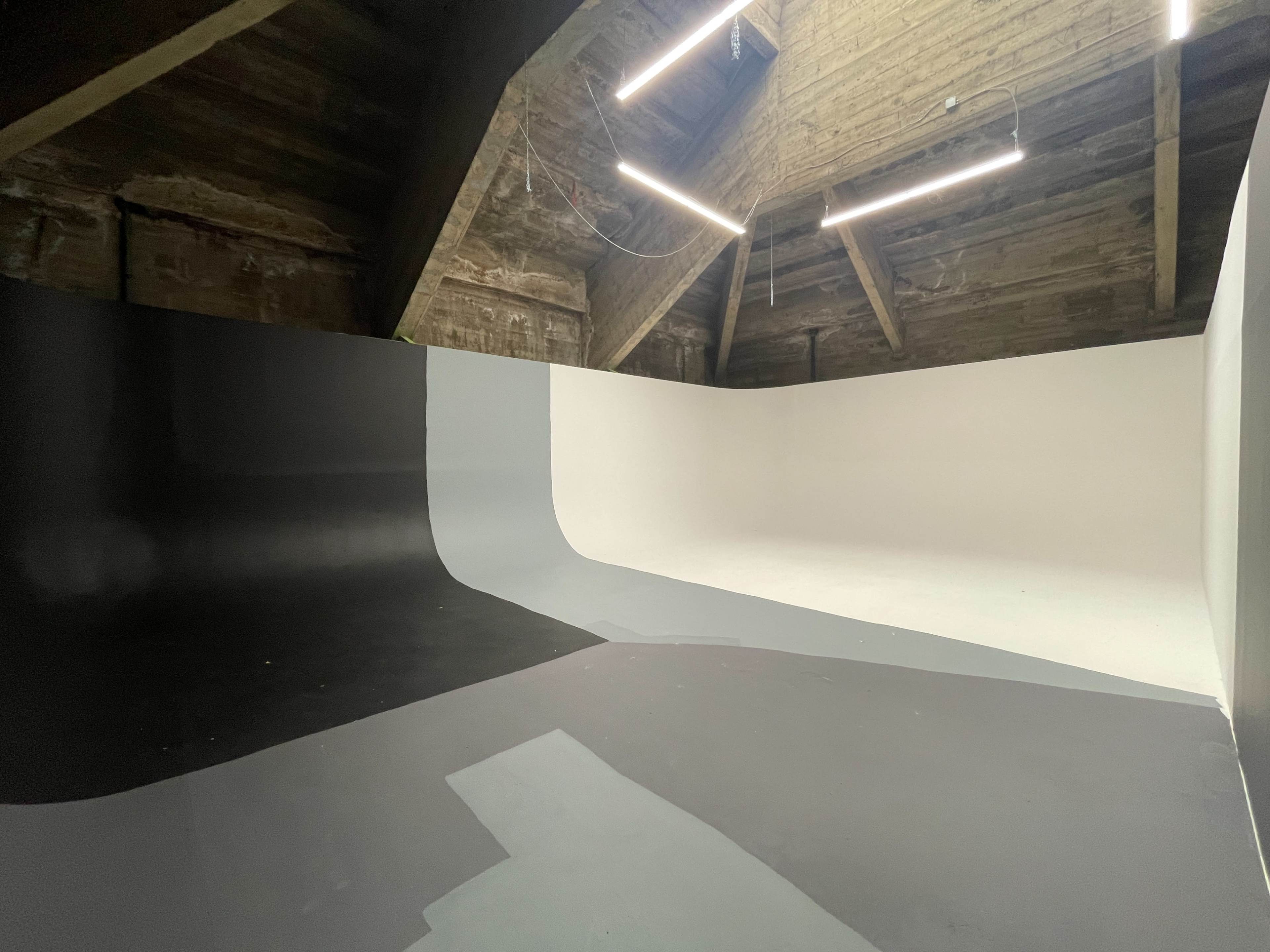 A modern photo studio with a curved backdrop painted in black, gray, and white, illuminated by overhead light fixtures.
