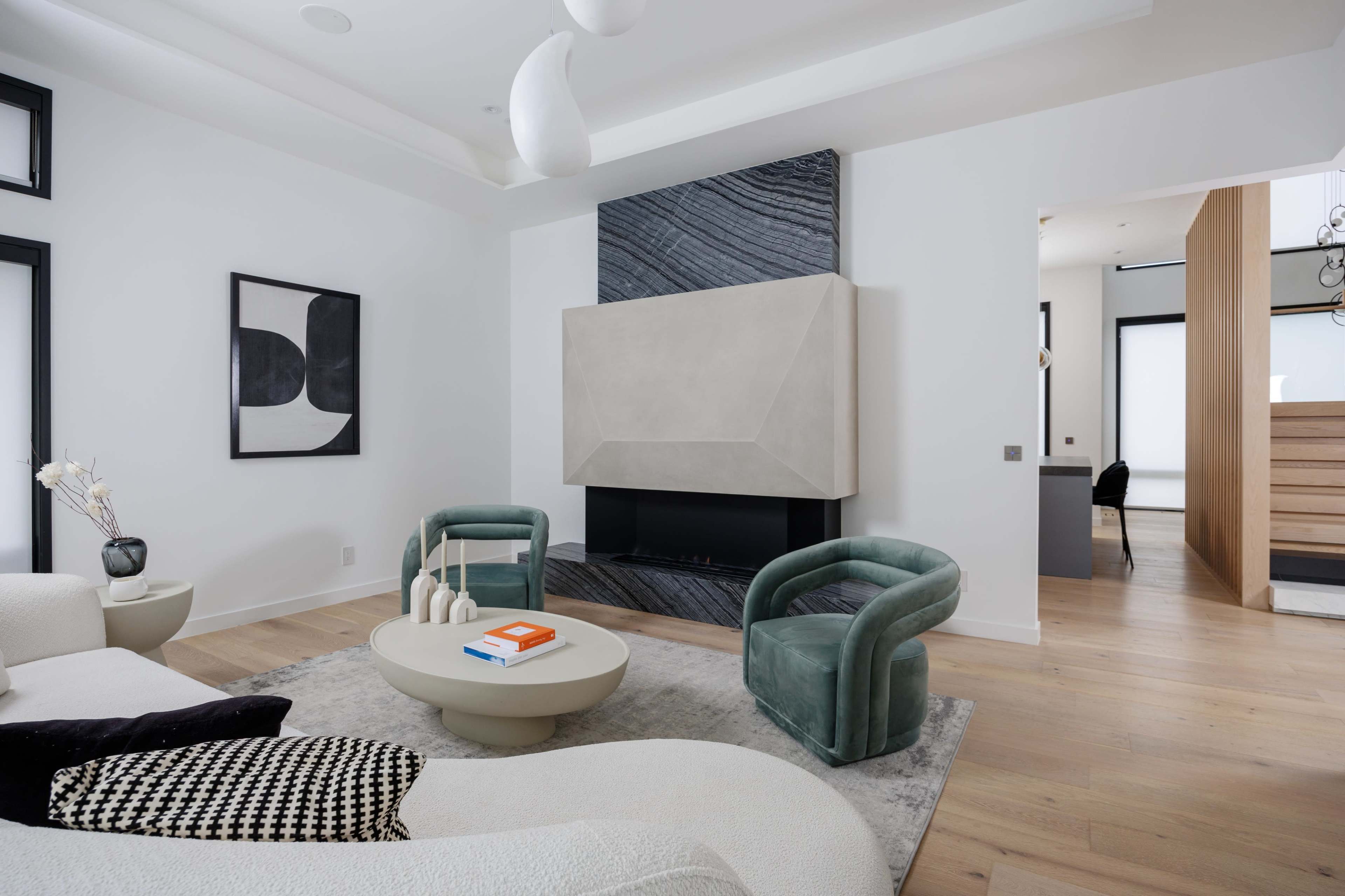 The scene features a modern living room with a minimalist design, showcasing a light-colored sofa, two green armchairs, a circular coffee table, and a statement fireplace against a textured wall.