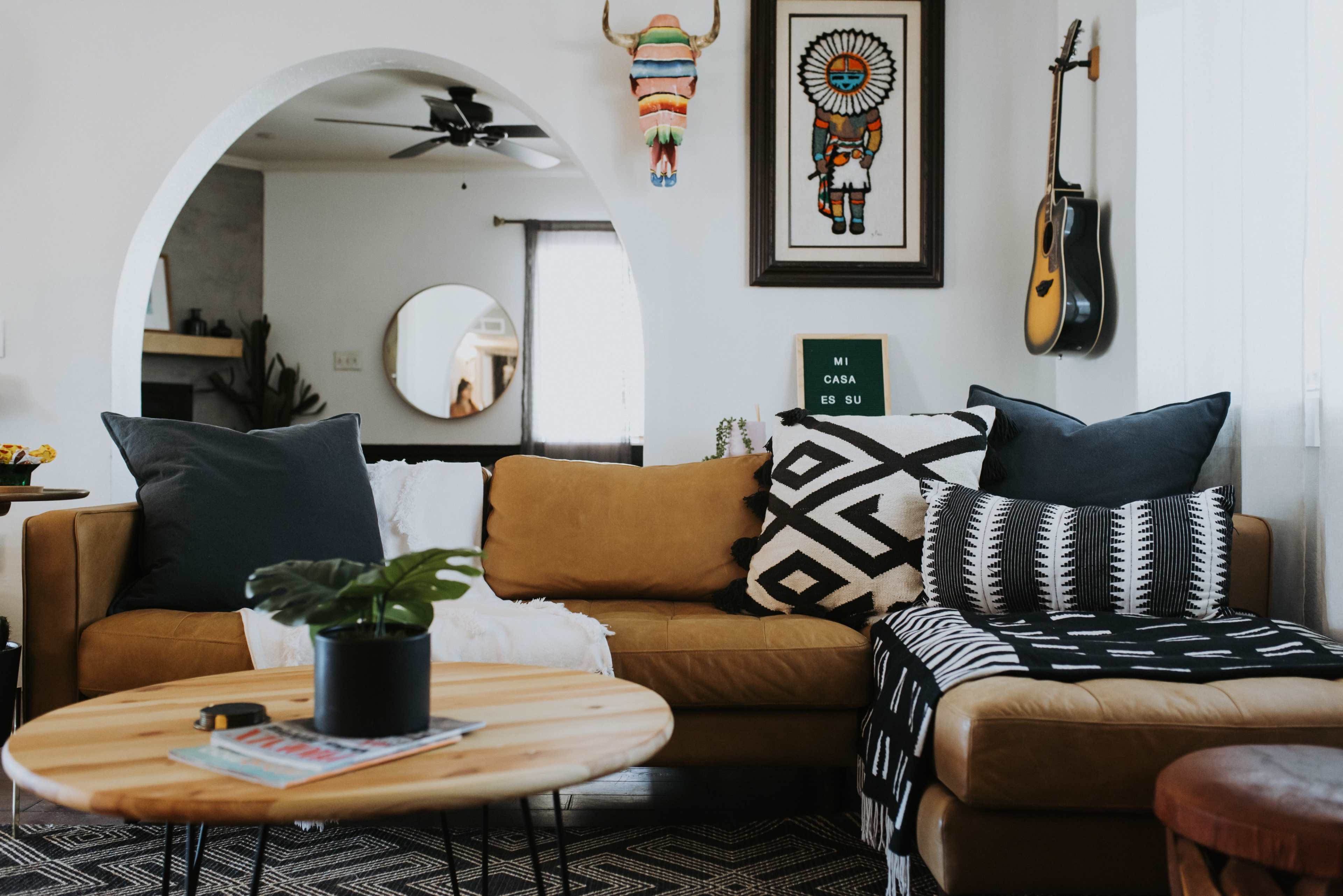 A cozy living room features a brown sofa with patterned pillows, a round wooden coffee table, and decor including artwork and a guitar.