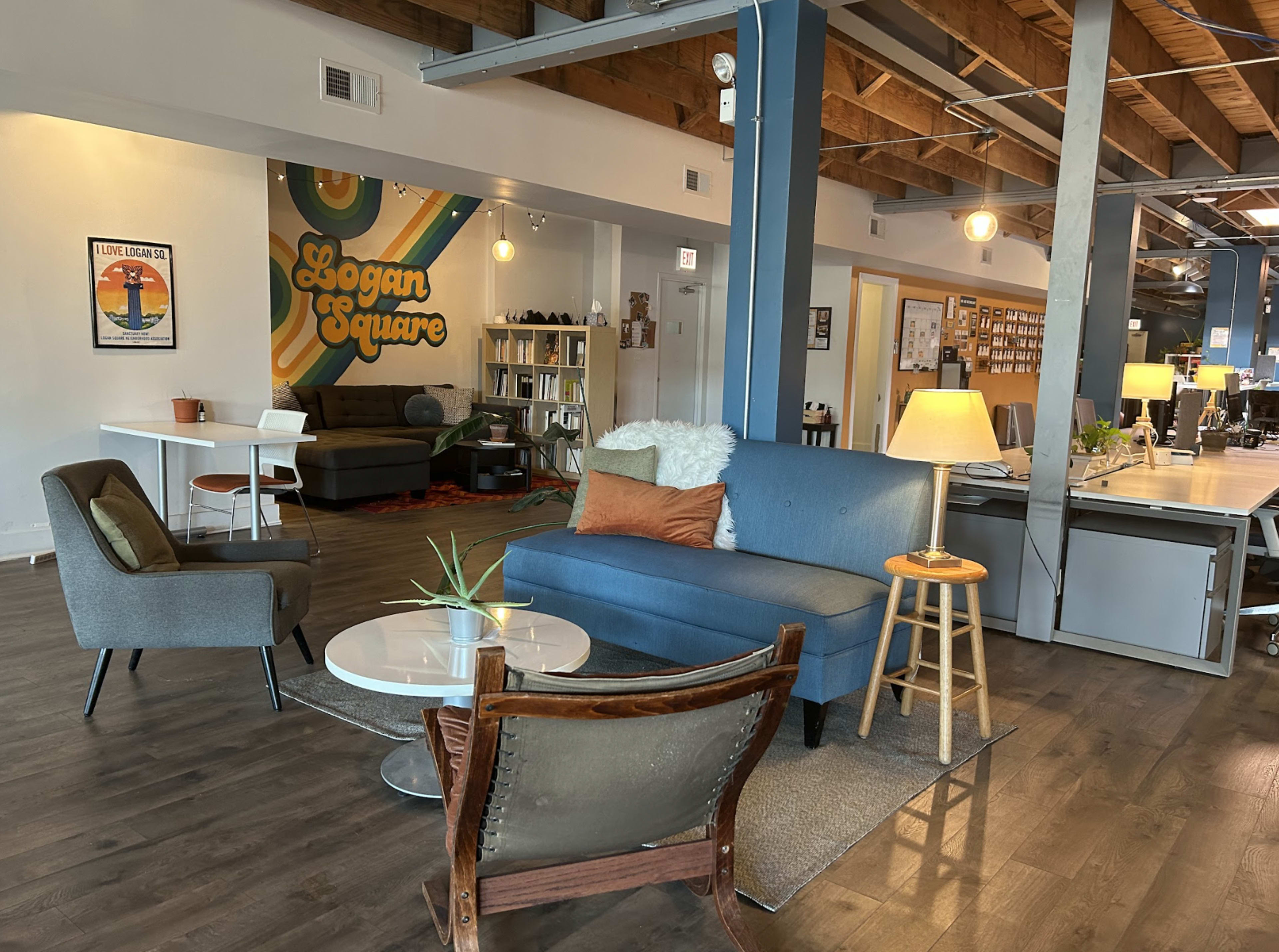 A modern workspace featuring a blue sofa, two armchairs, a coffee table, and a decorative wall with "Logan Square" written on it.