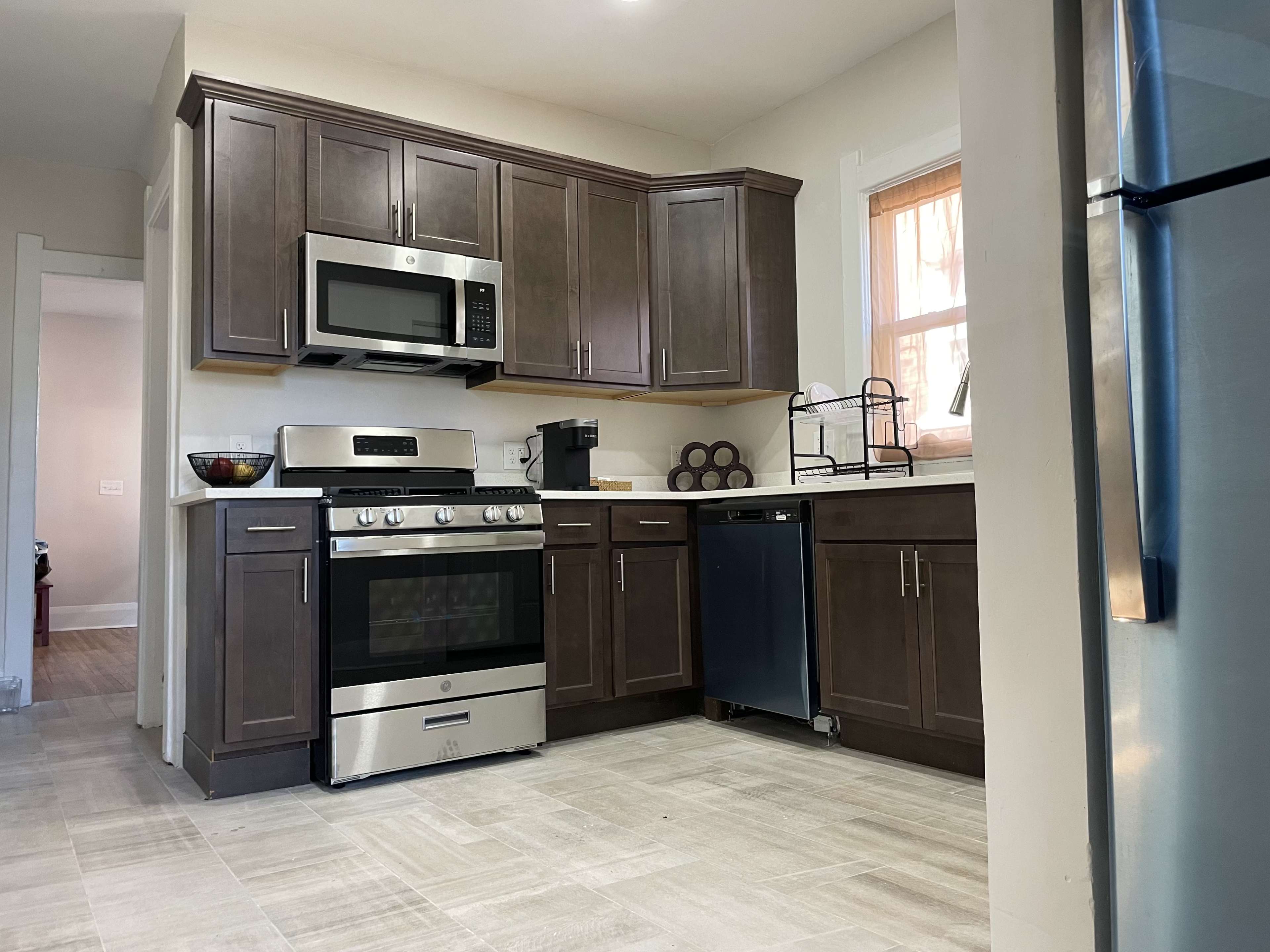 A modern kitchen with dark wood cabinets, a stainless steel stove and microwave, and a silver dishwasher.
