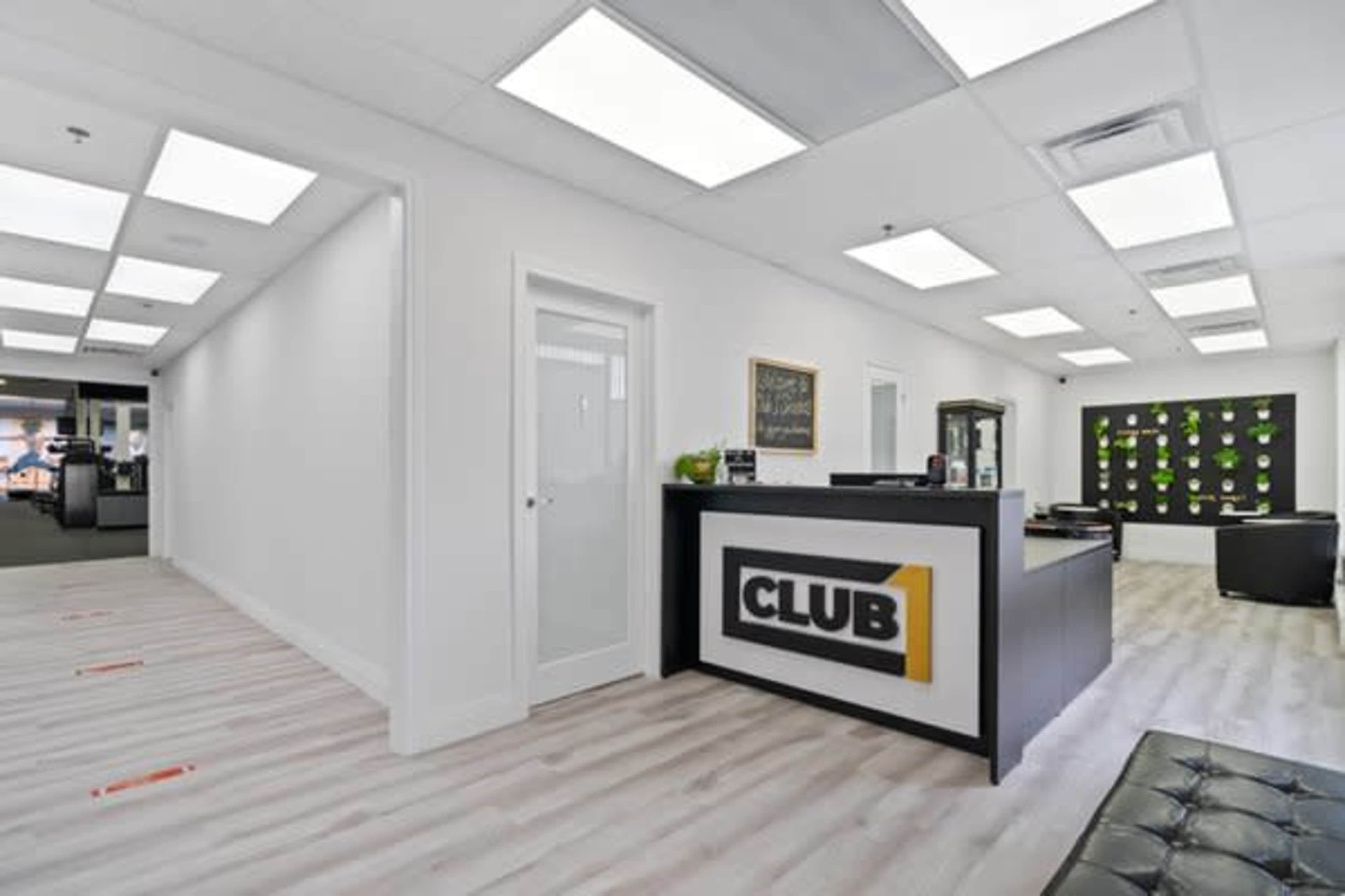 A modern office reception area with a black front desk labeled "CLUB 1" and sleek, white walls.