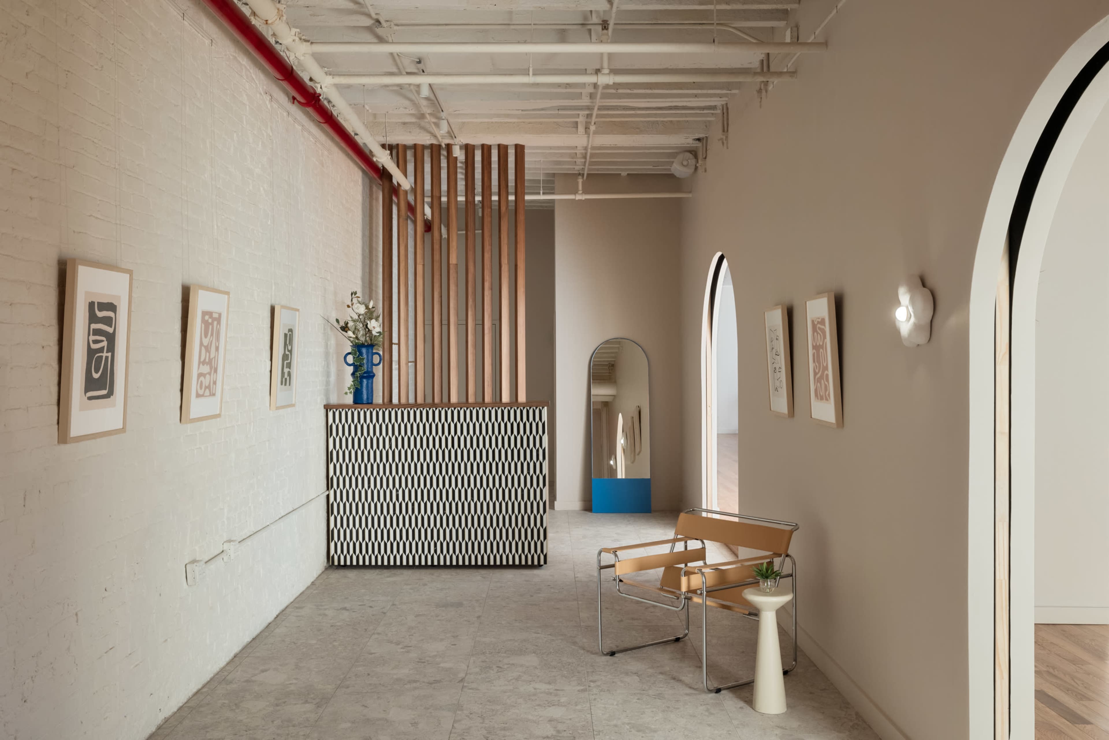 A modern interior space featuring a reception area with a geometric counter, arched doorway, framed artwork on the walls, and minimalist furniture.