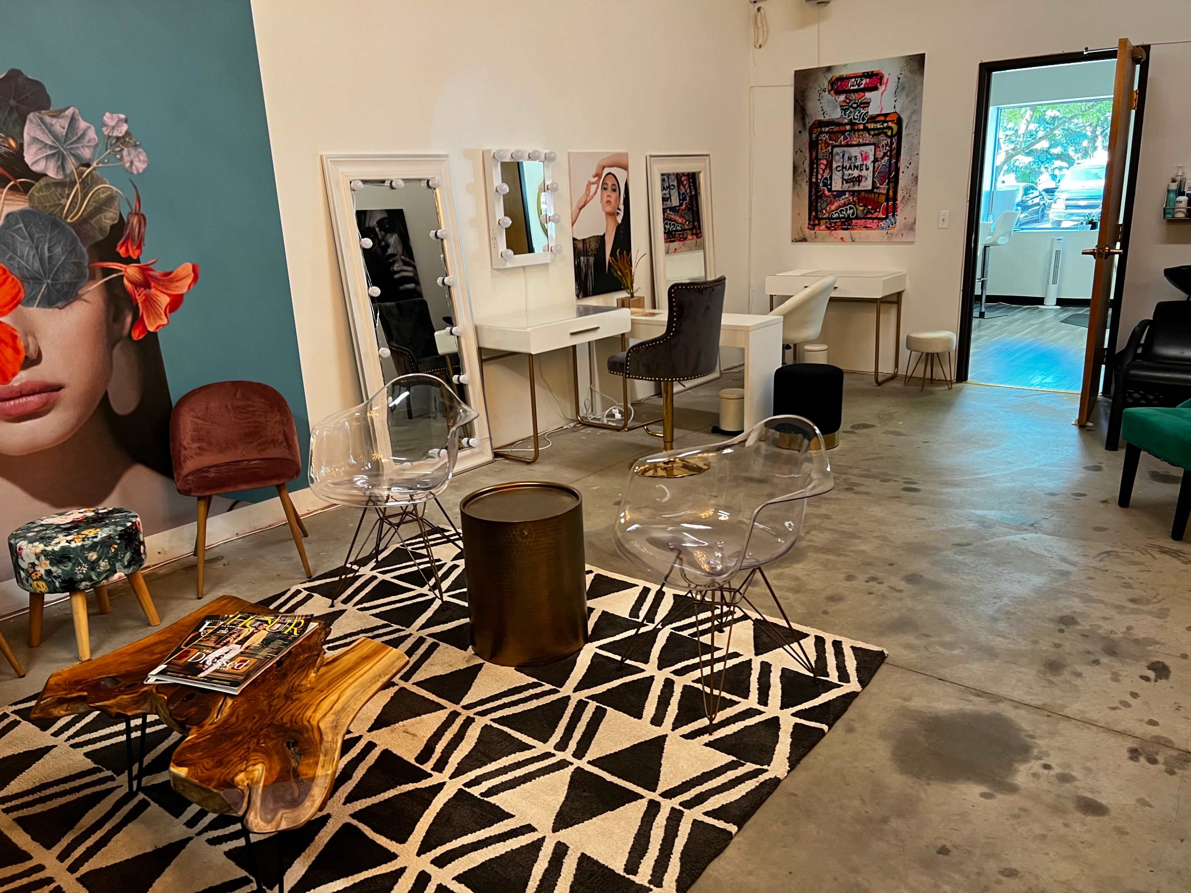 A salon interior with a seating area featuring a patterned rug, various chairs, and makeup stations lined against the wall.