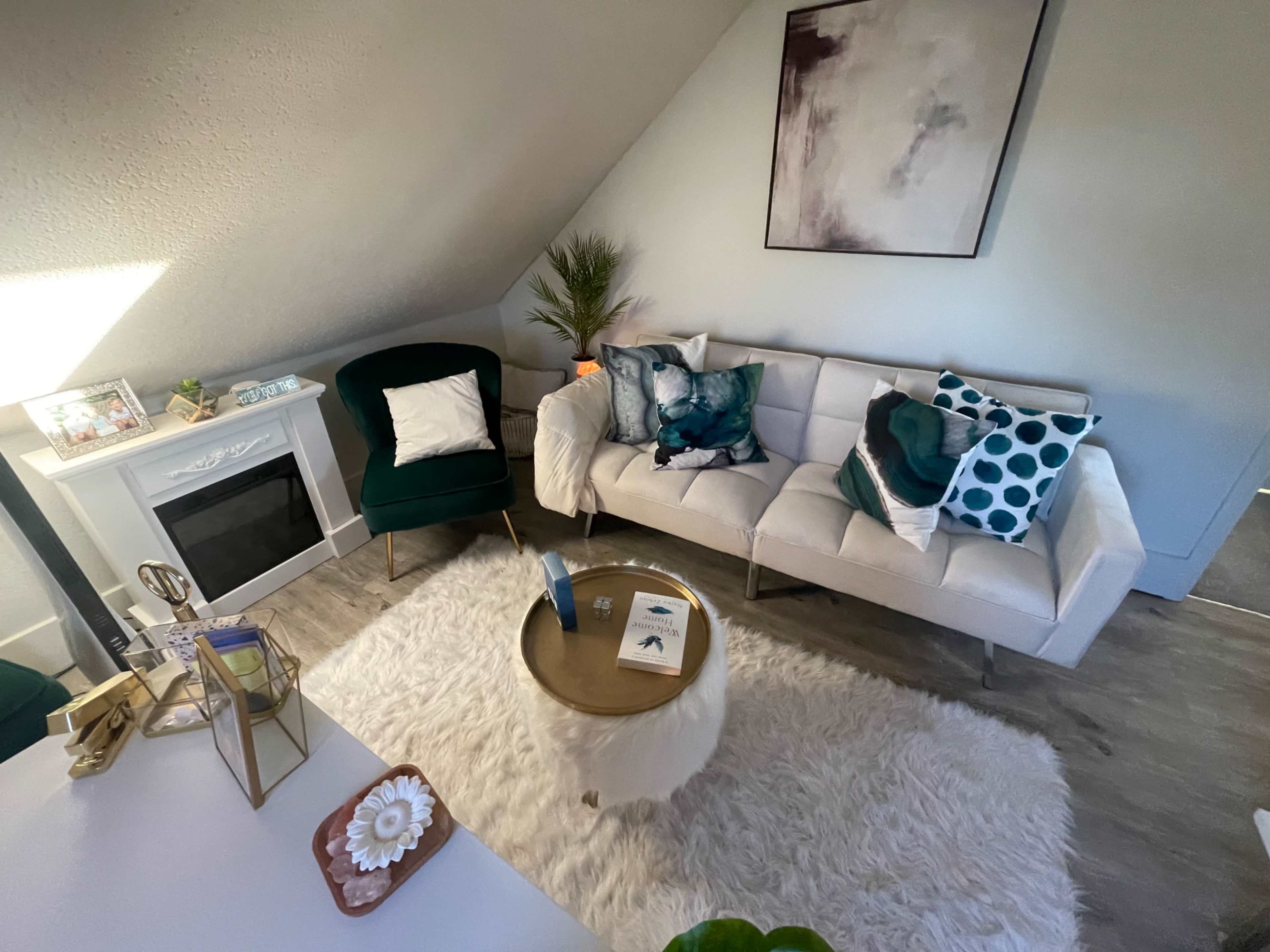 A modern living room features a sectional sofa with decorative cushions, a round coffee table on a plush rug, and a small electric fireplace.