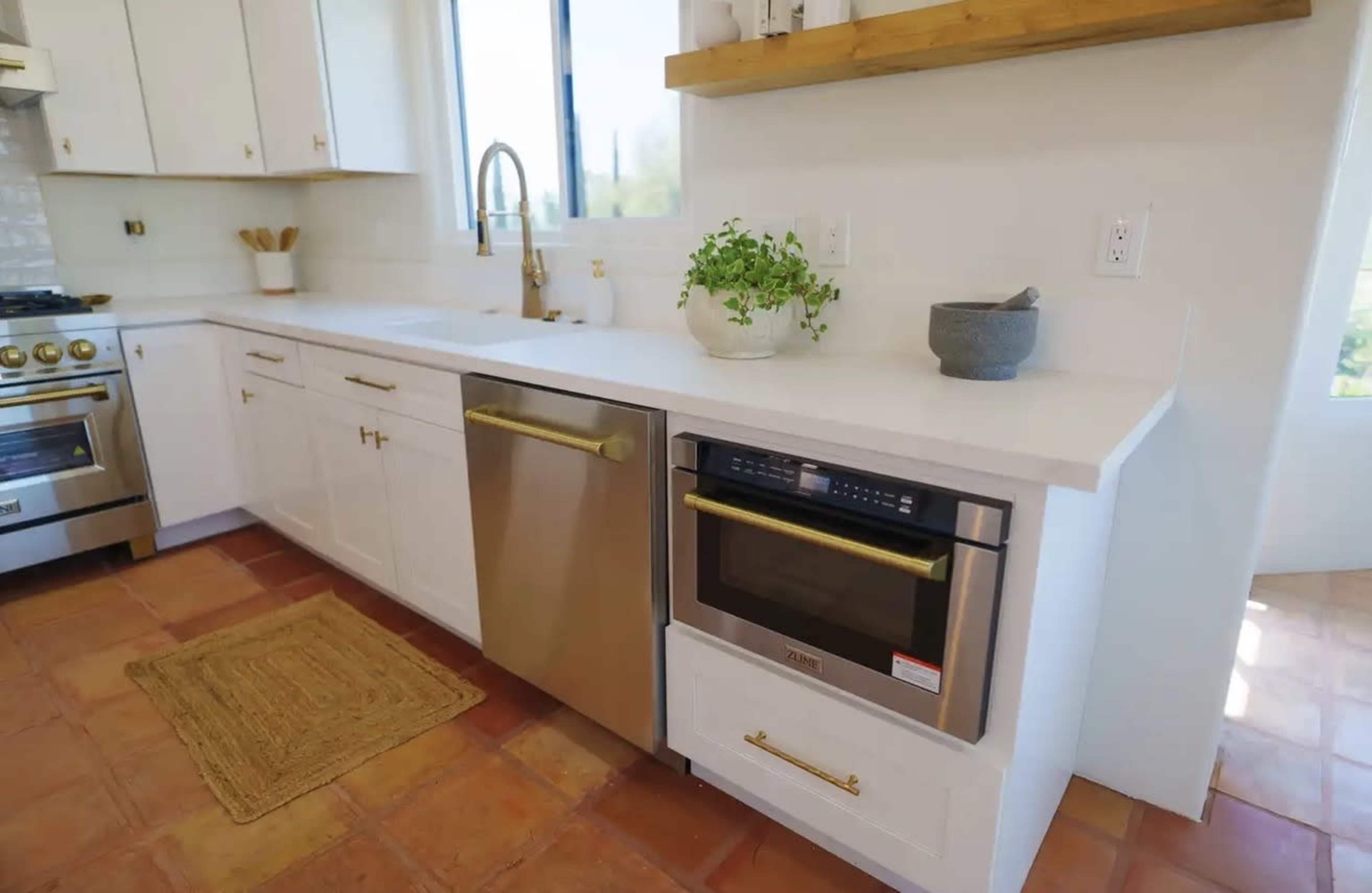 The image shows a modern kitchen with white cabinets, a stainless steel dishwasher, a built-in oven, and a window above the sink.