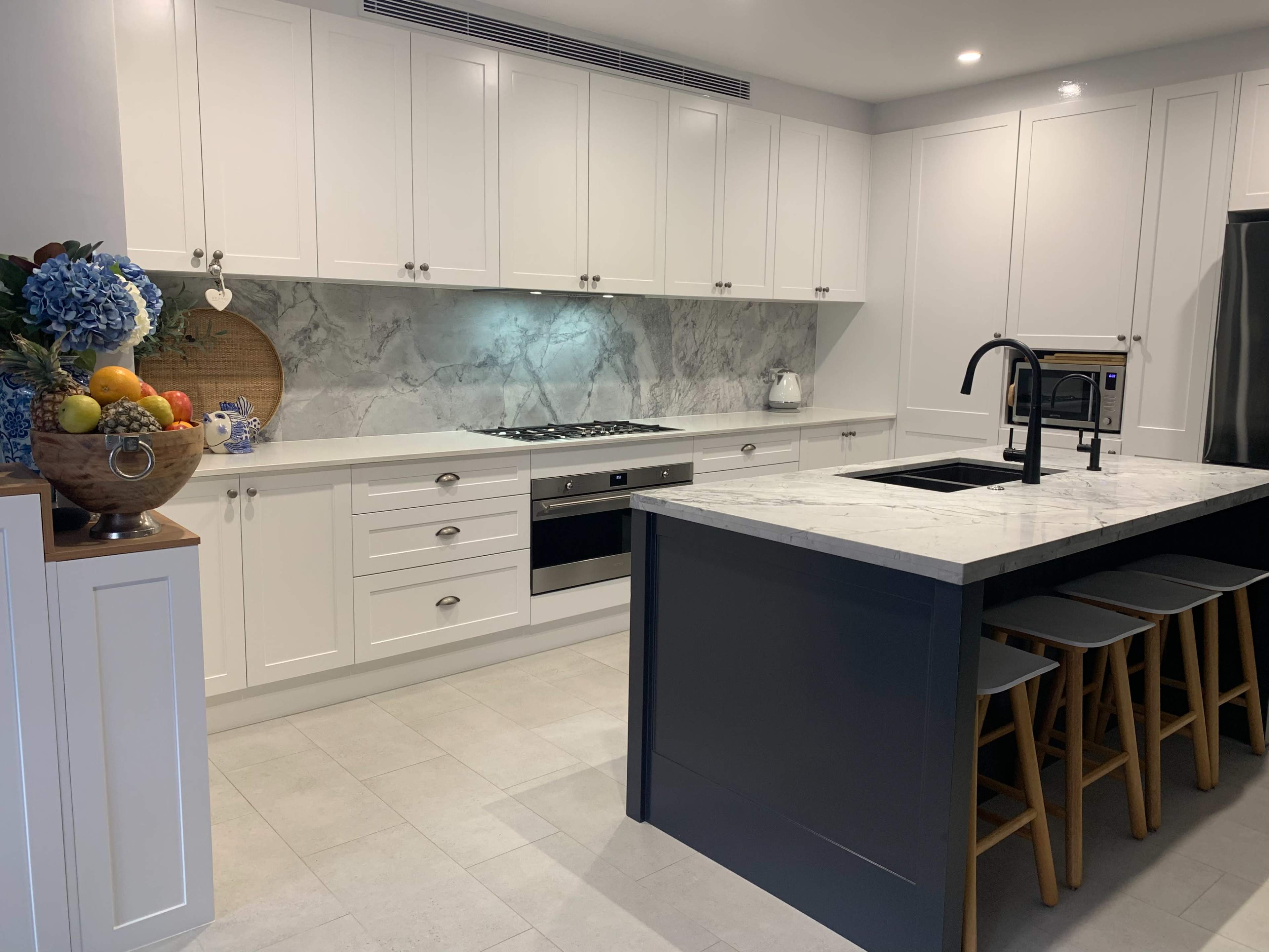 The kitchen features white cabinetry, a marble backsplash, a central island with a marble countertop, and wooden stools lined up in front.