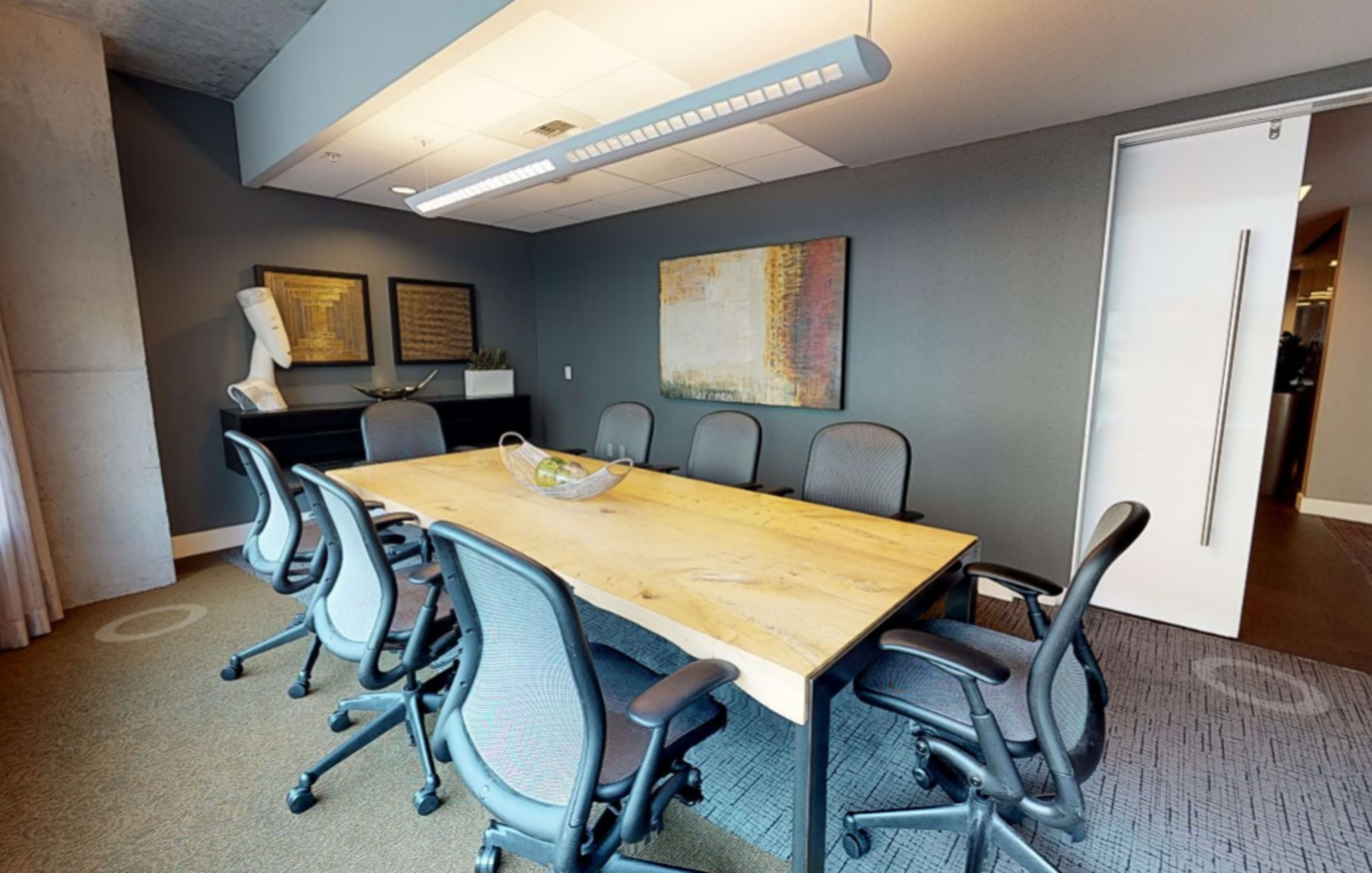 A conference room features a large wooden table surrounded by ergonomic chairs, with artwork on the walls and a decorative piece in the background.