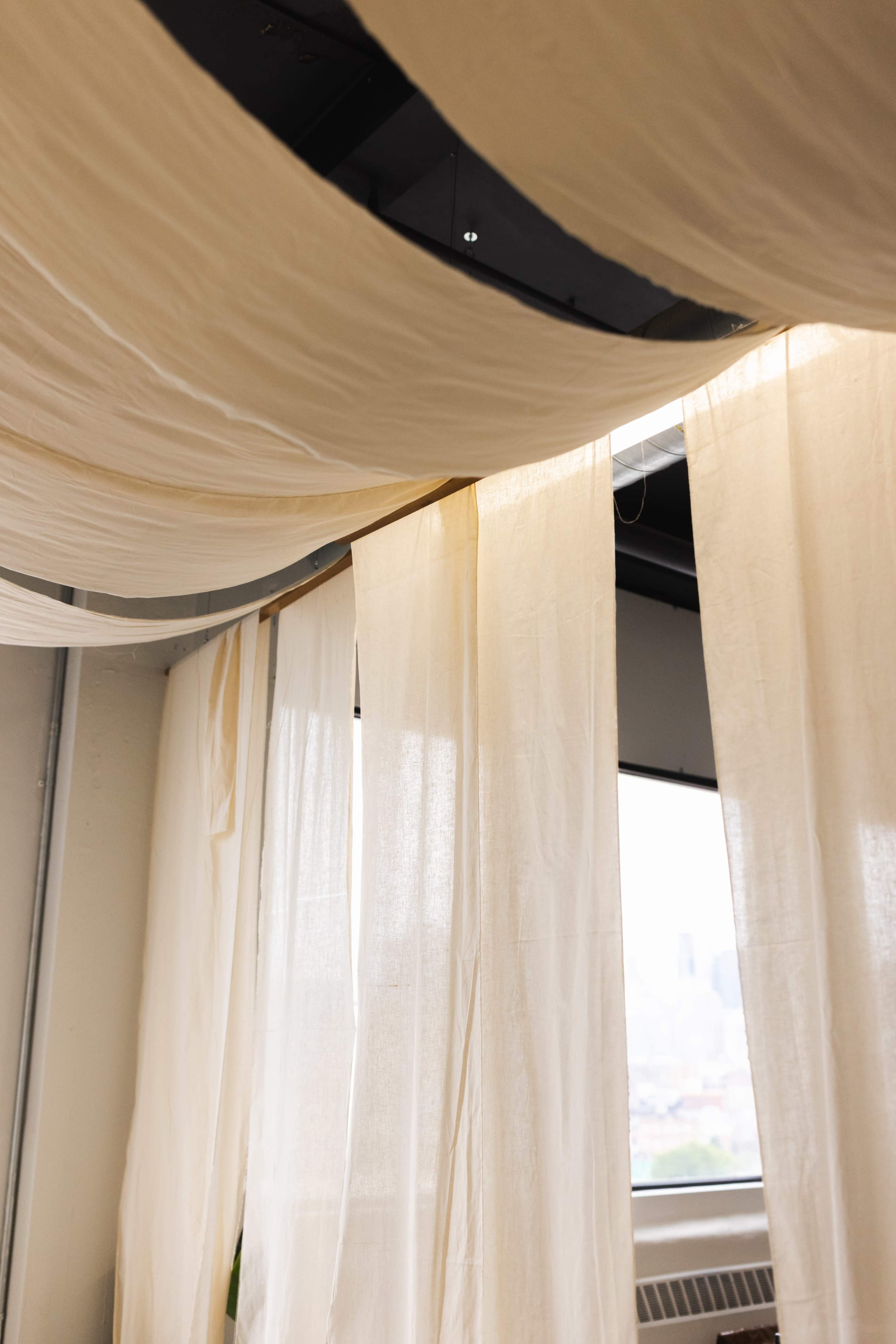 Sheer fabric panels hang from the ceiling, partially obscuring a window with a city view in the background.