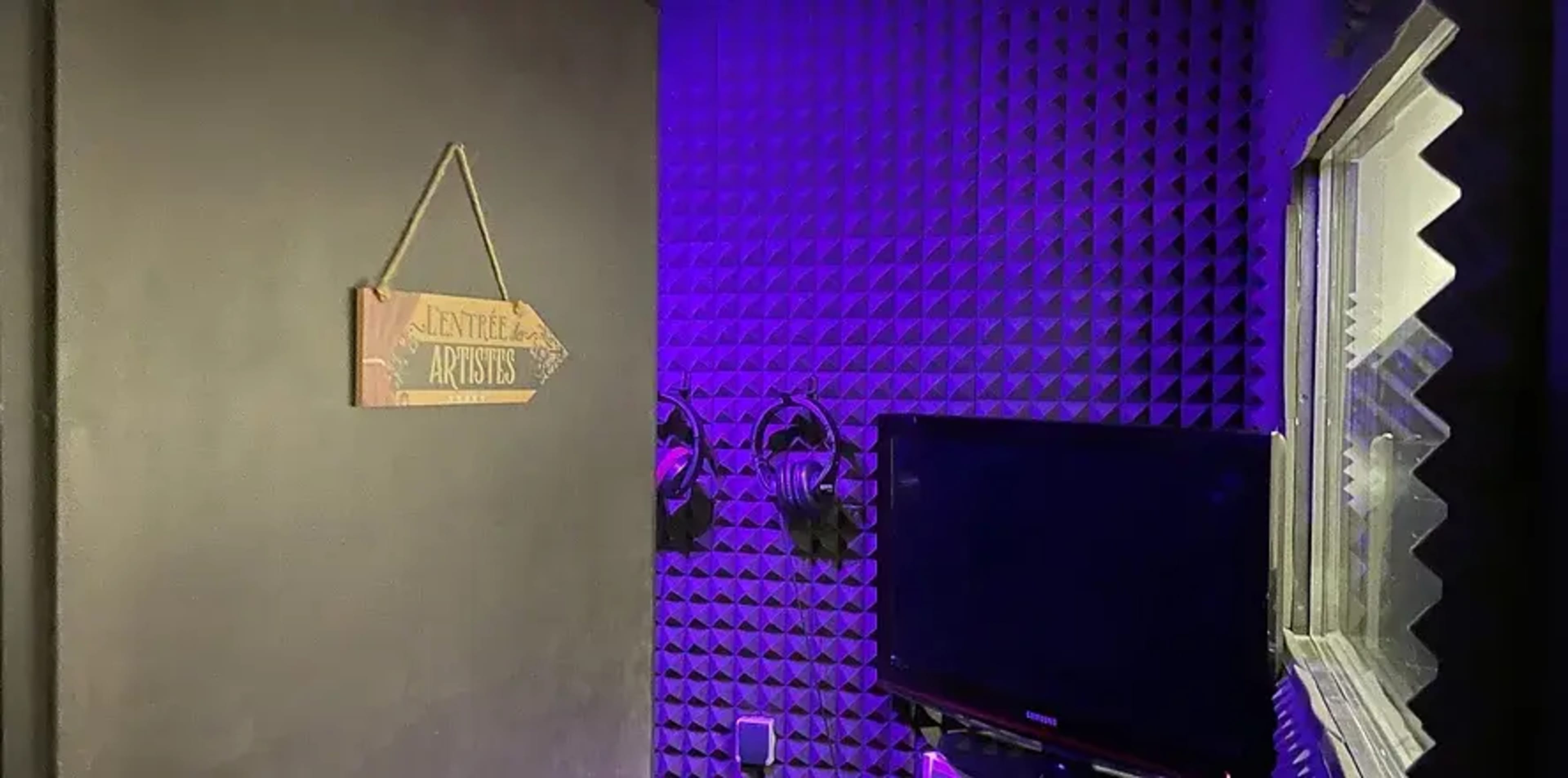 A small room featuring soundproofed walls, a sign labeled "Artists," a television, and two mounted headphones.